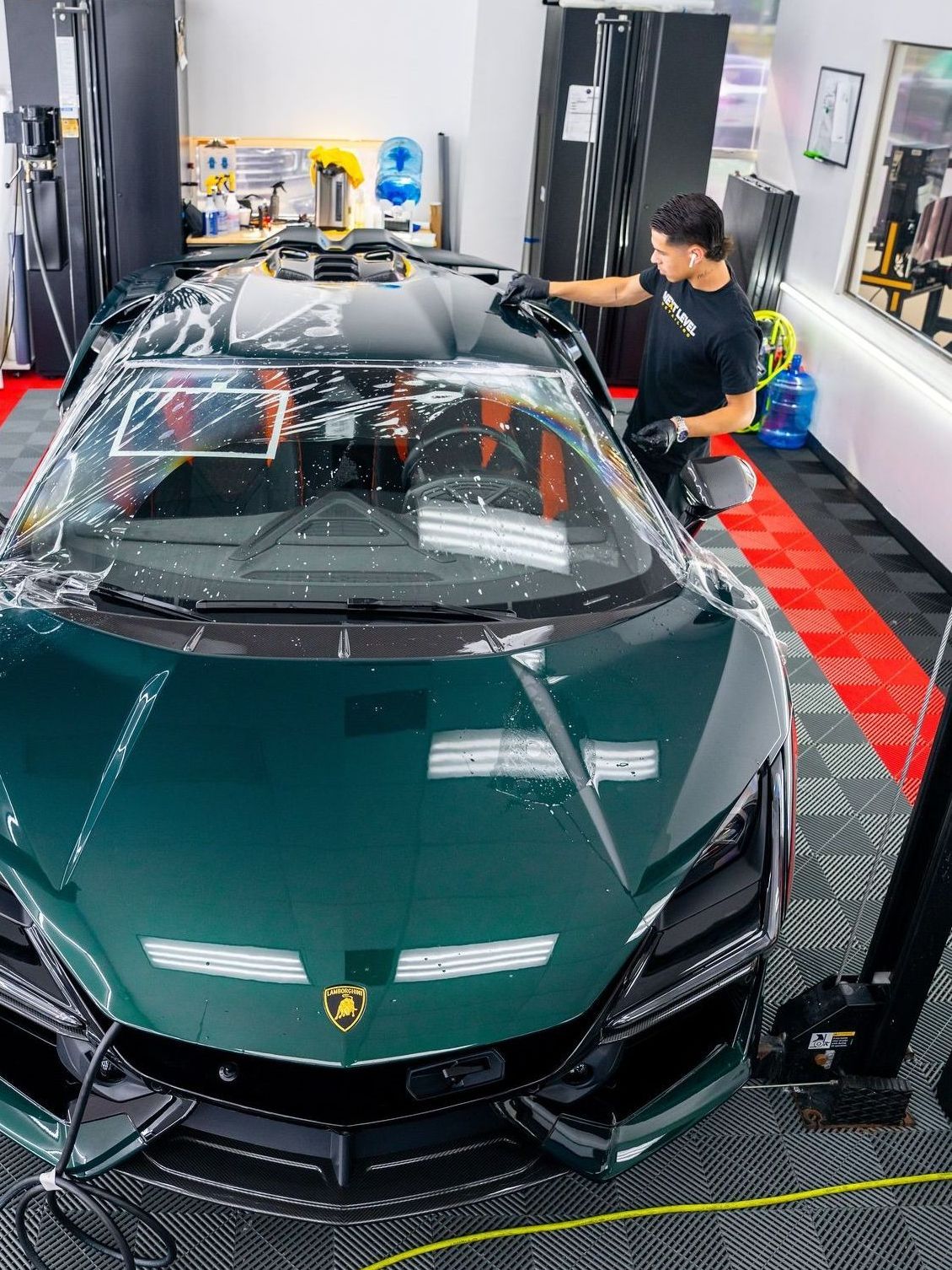 Man washing a dark green Lamborghini inside a garage, using soapy water.