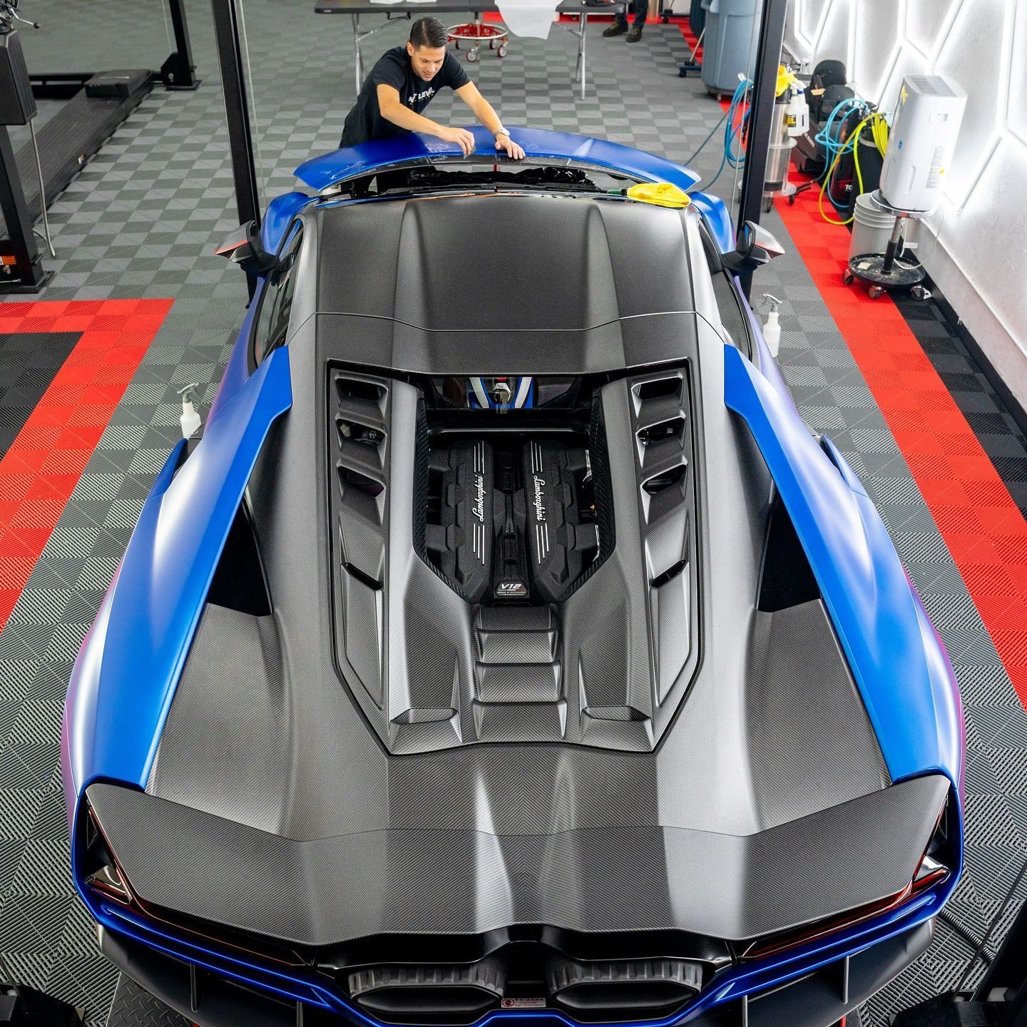A black car is on a lift in a garage with the word xpel on the wall