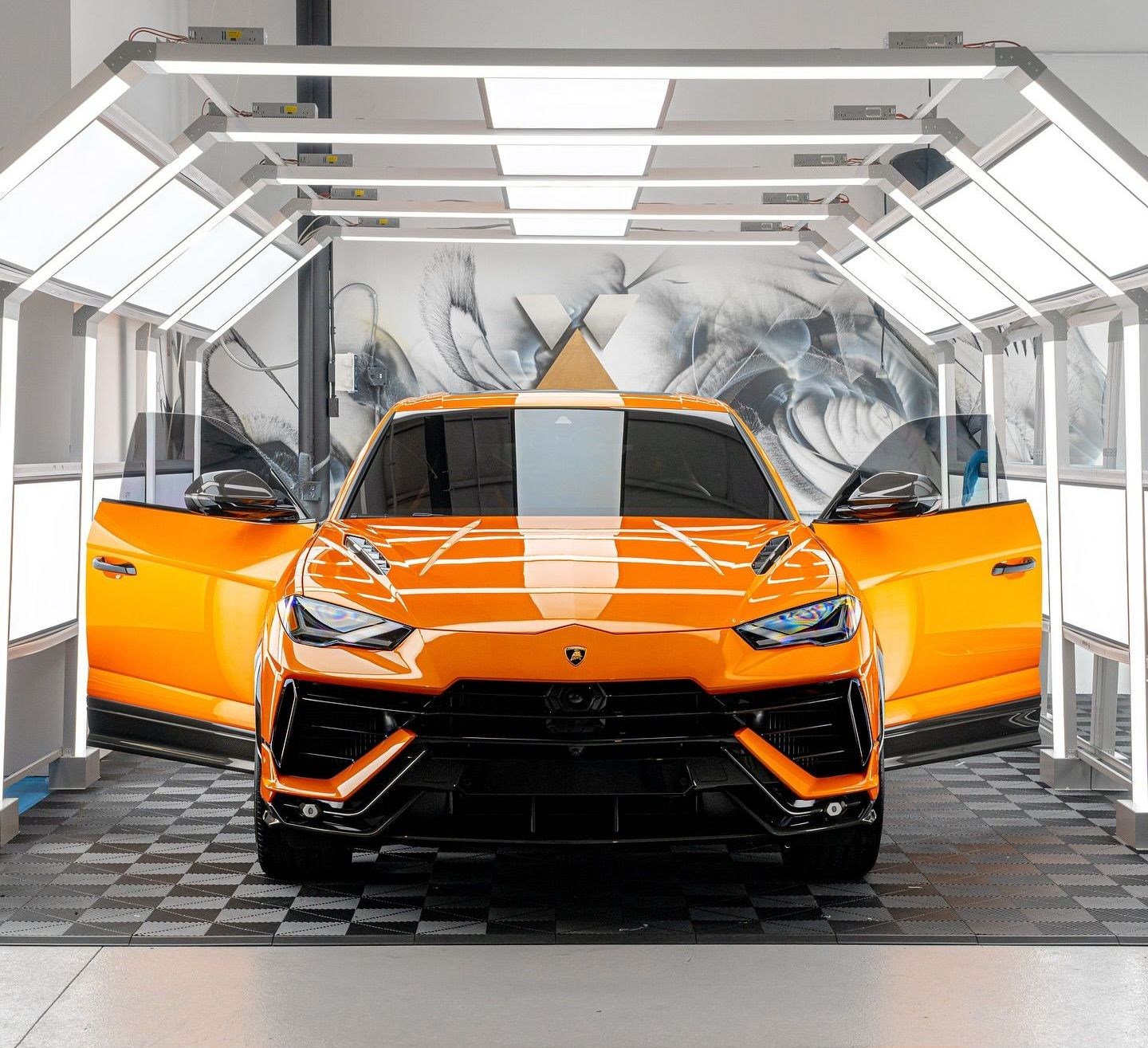 Orange Lamborghini SUV with open doors, in a brightly lit car detailing bay.