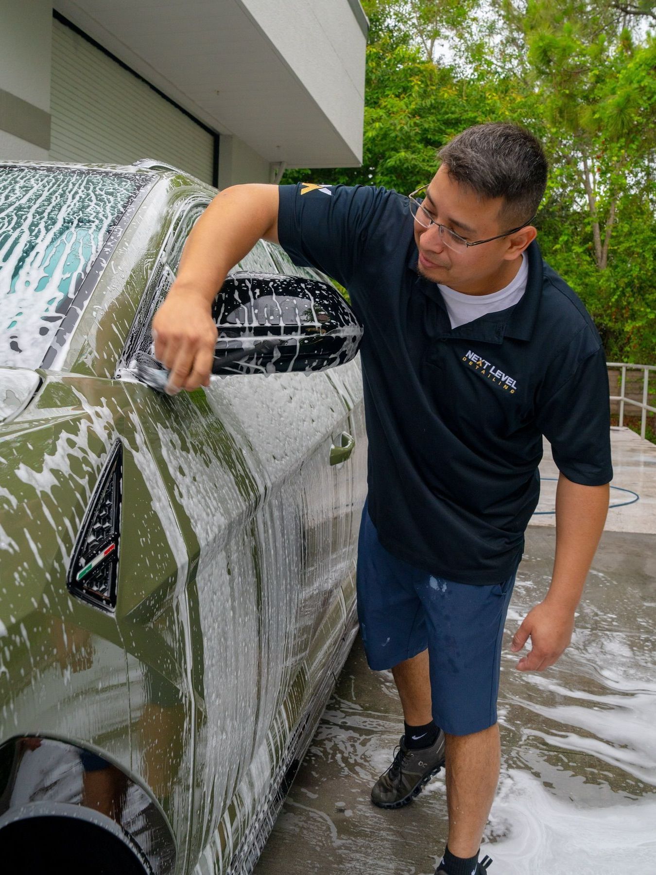 A man is washing a yellow car in front of a building.