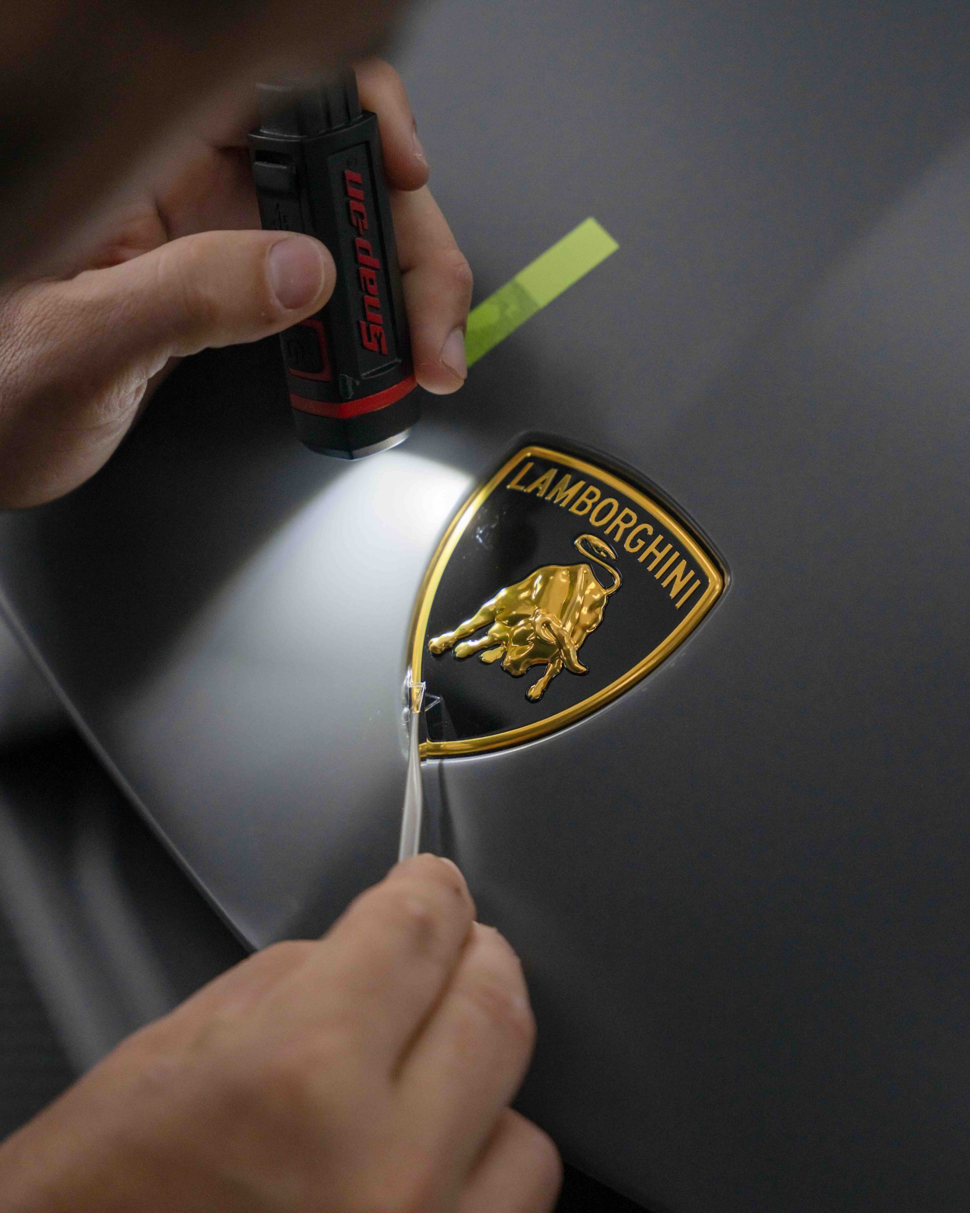 A person is working on a lamborghini emblem with a flashlight