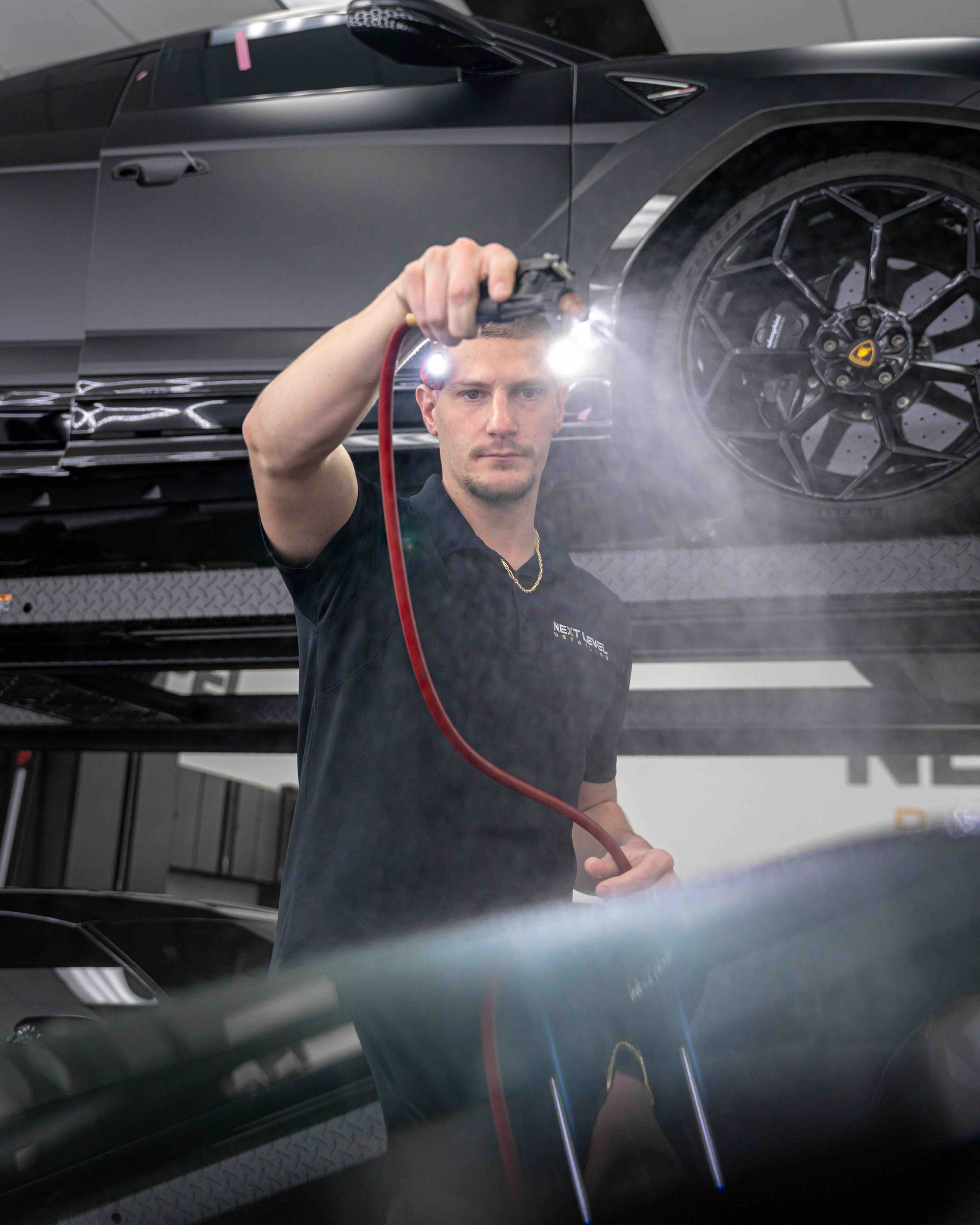 A man is spraying a car with a hose in a garage.