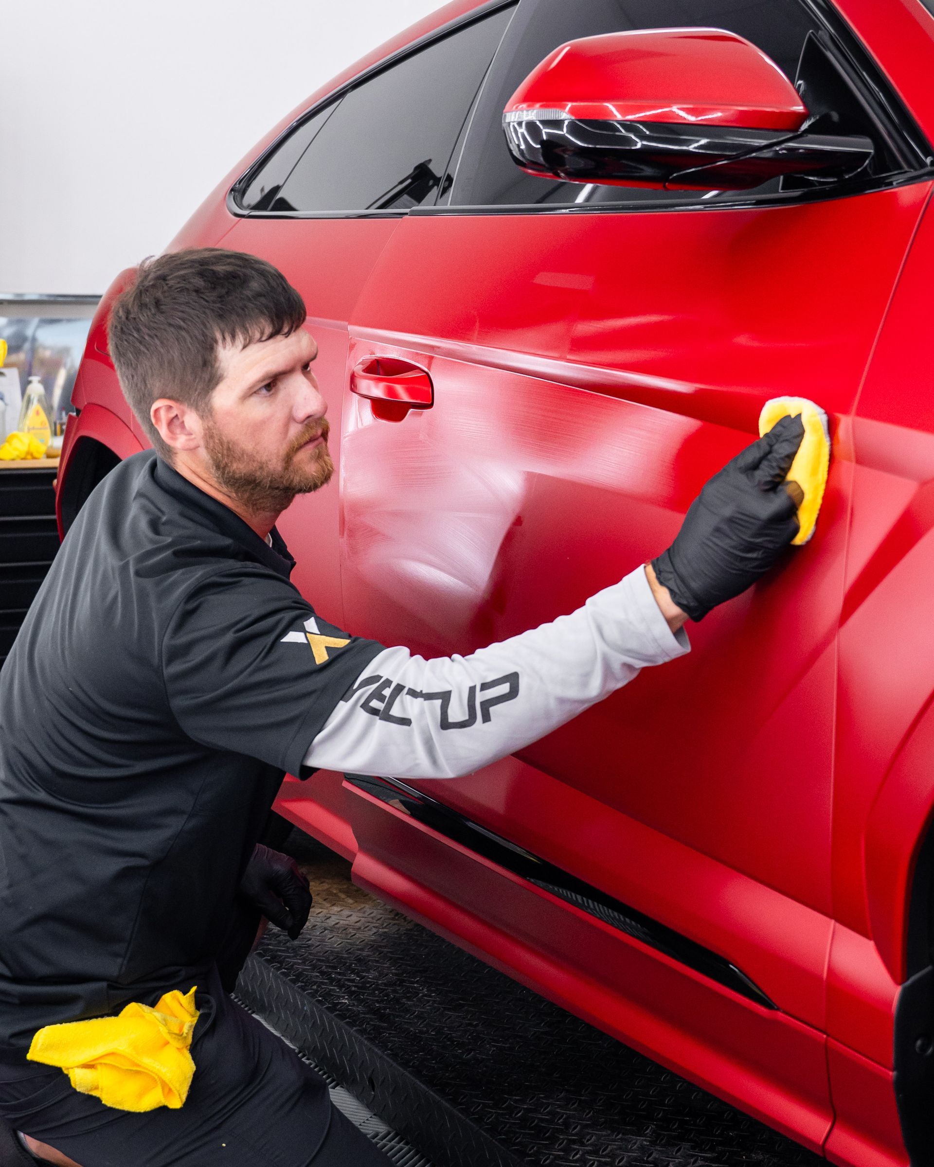 A man is cleaning a red car with a sponge.