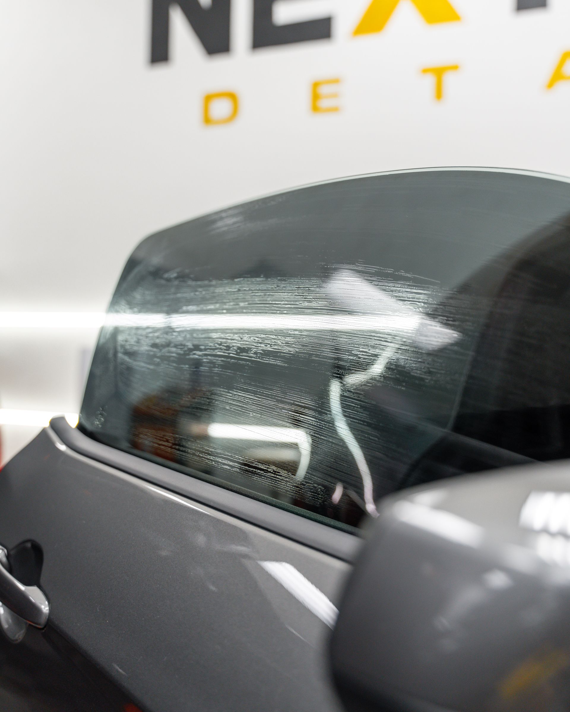 A close up of a car window with a nex detail logo in the background