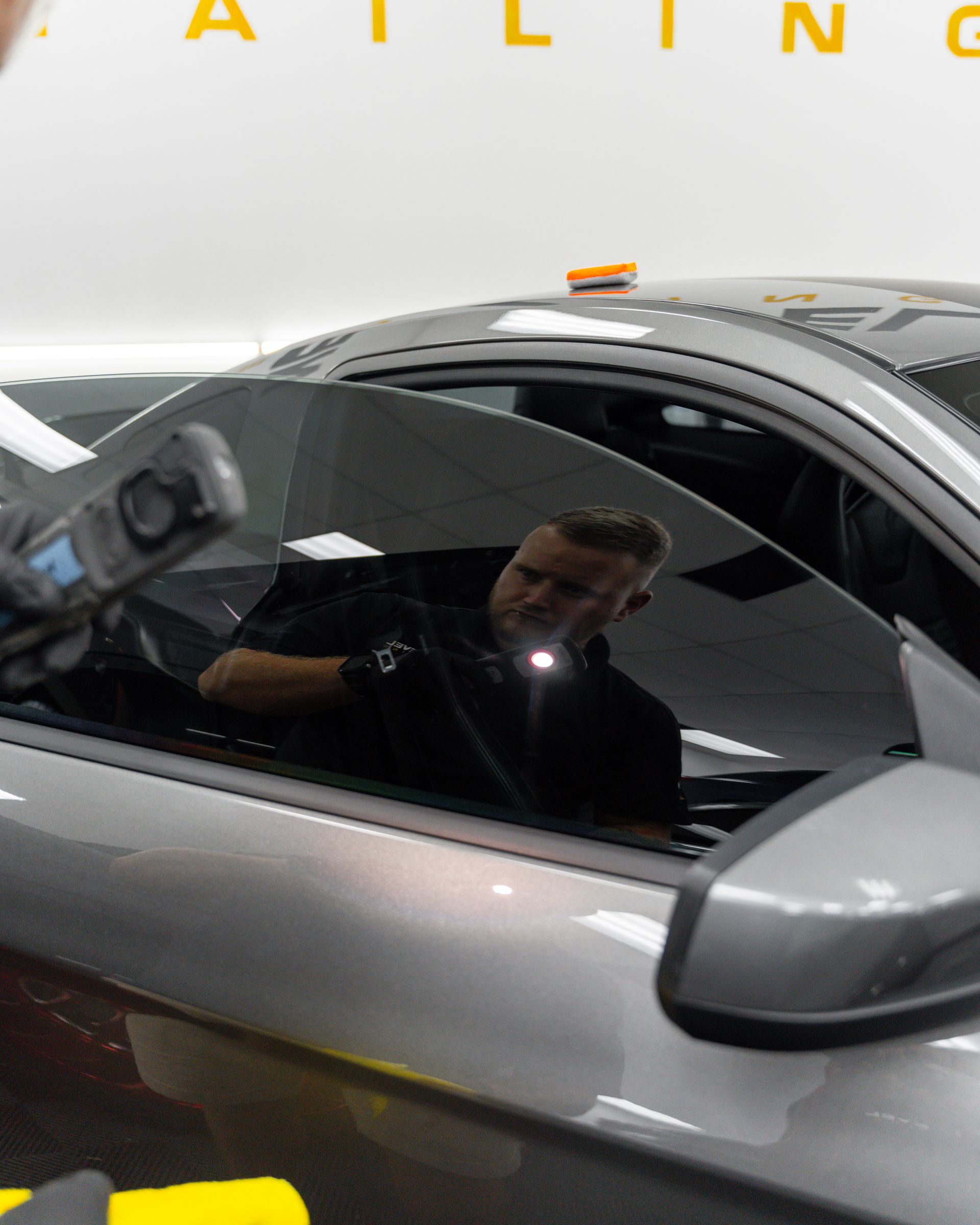 A man is reflected in the window of a silver car