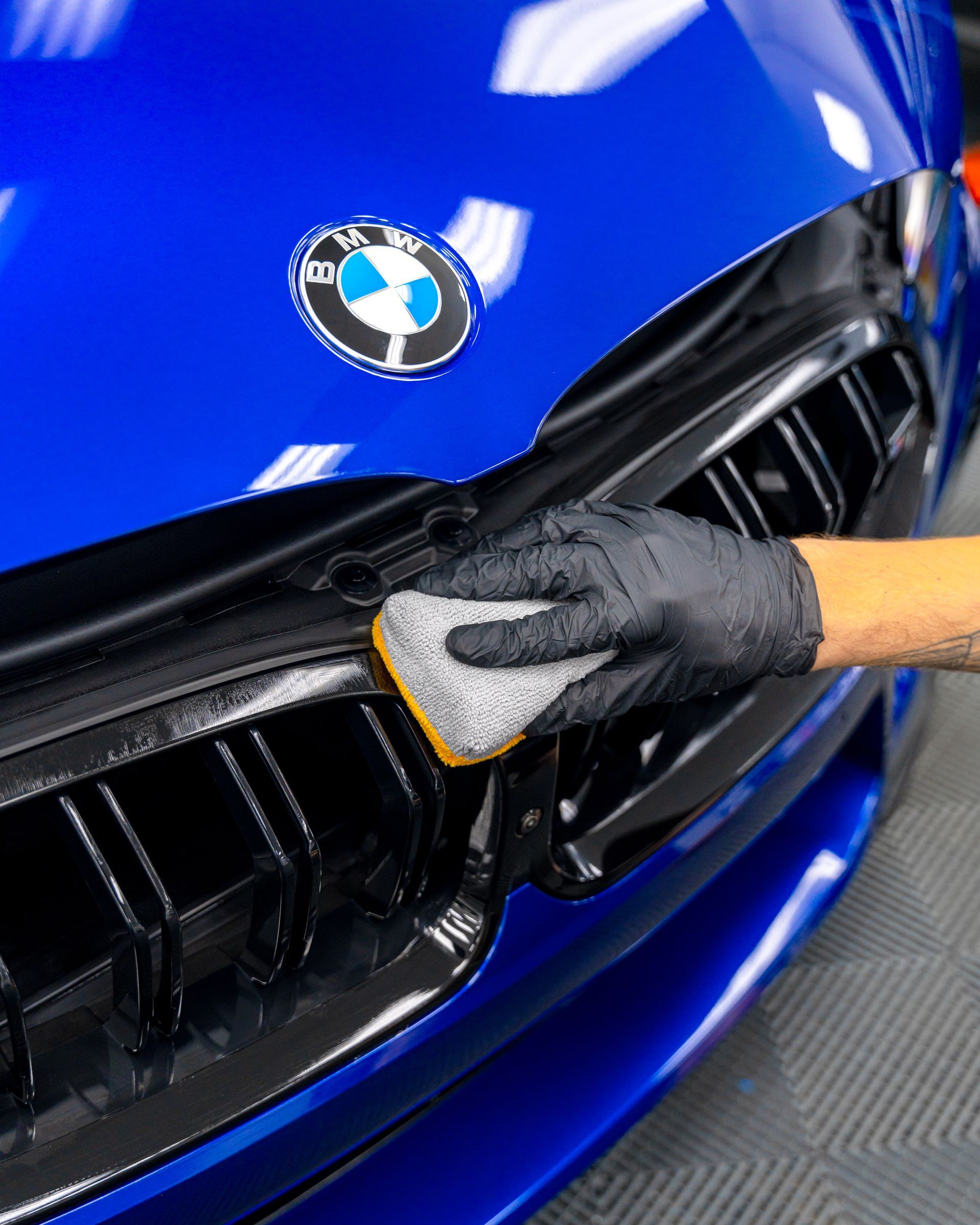 A person is cleaning the front of a blue bmw with a sponge.
