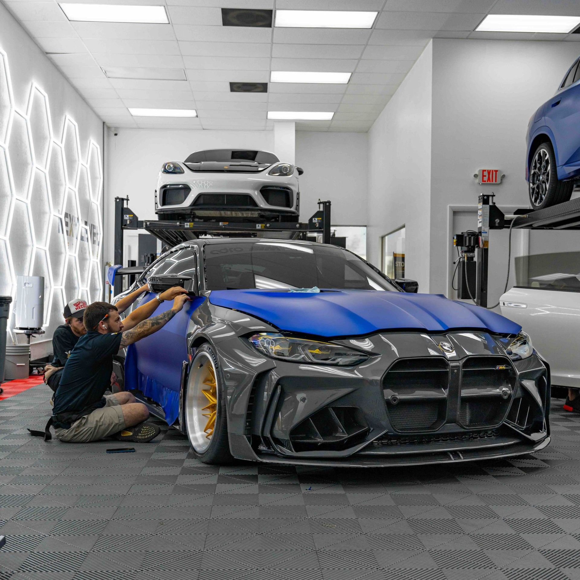 Two men are working on a blue car in a garage.