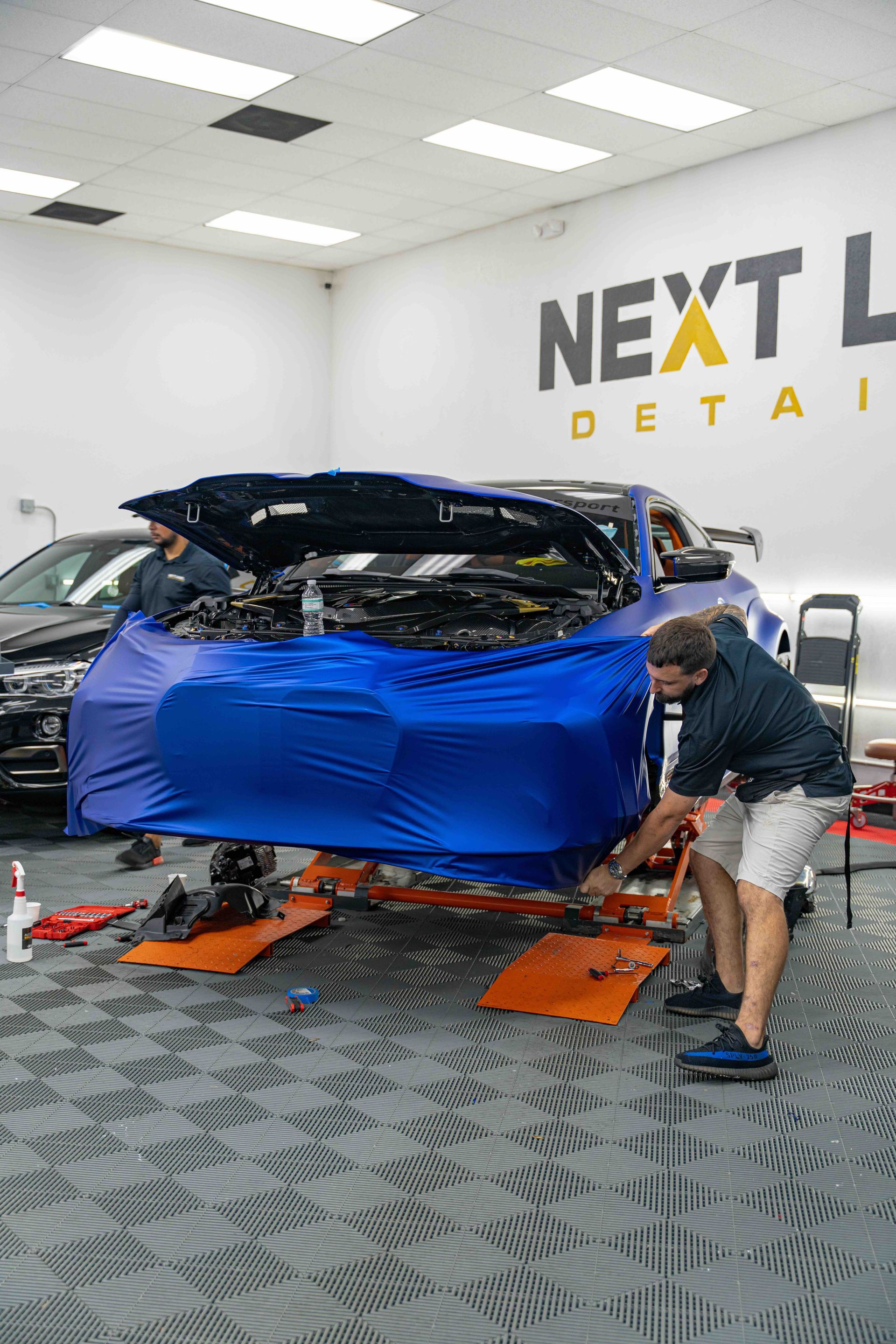 A man is wrapping a car in blue plastic in a garage.