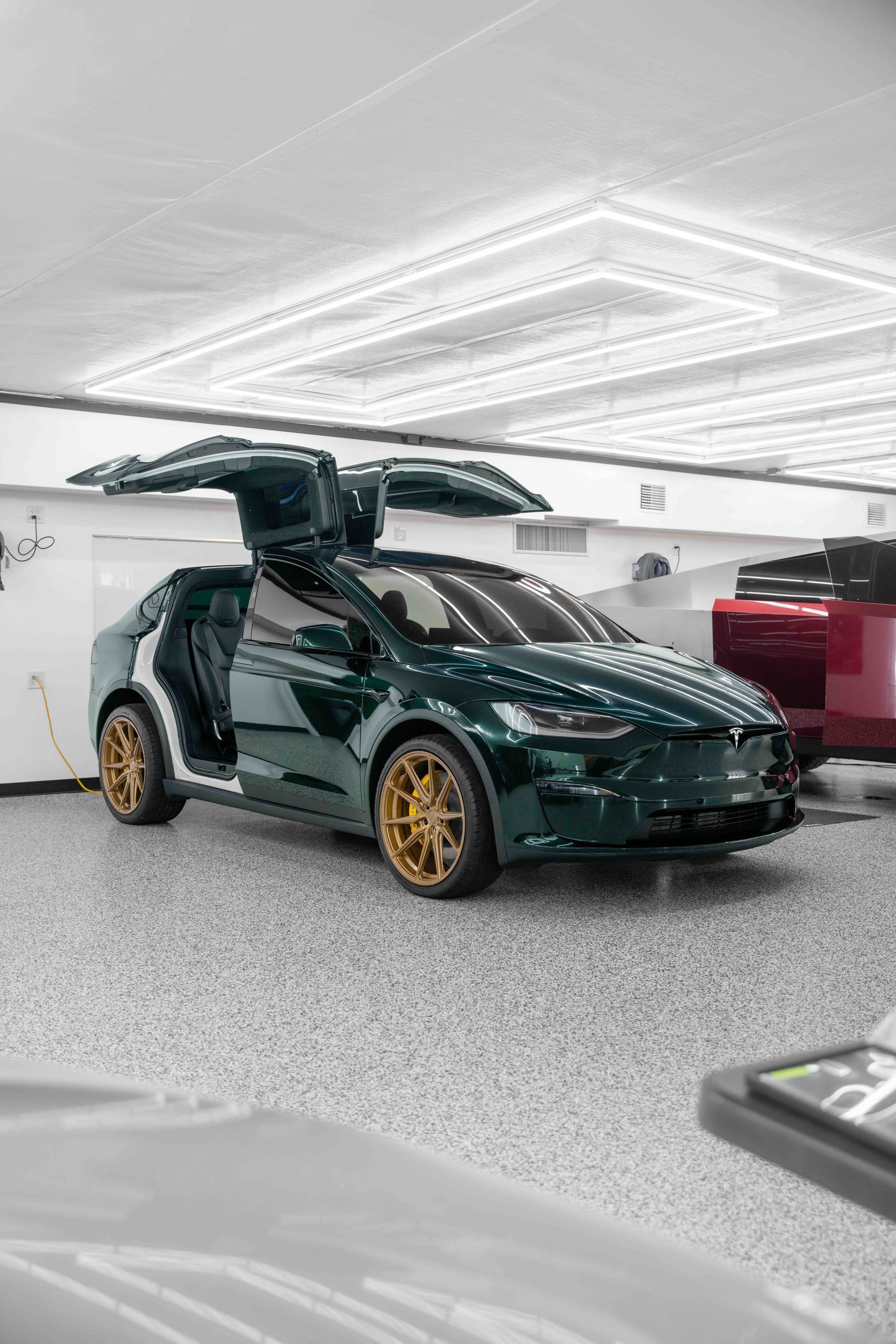 A green tesla model x is parked in a garage with its doors open.