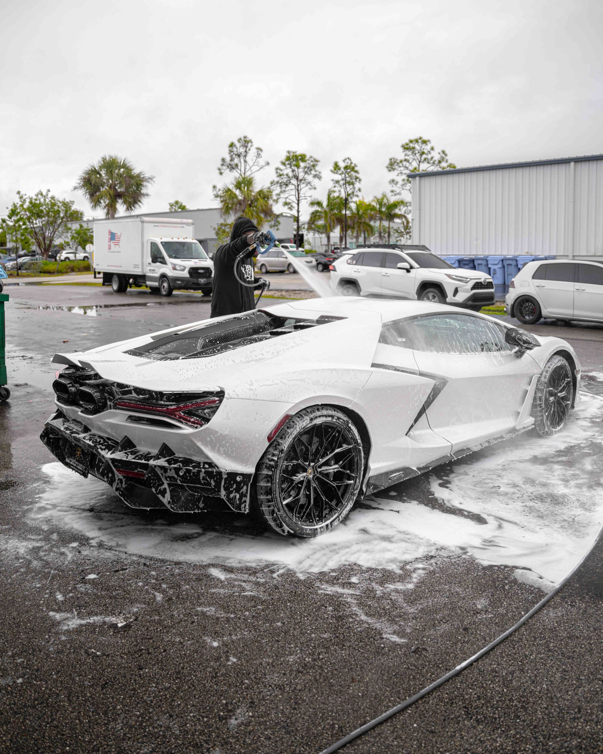 A man is washing a white sports car with foam.
