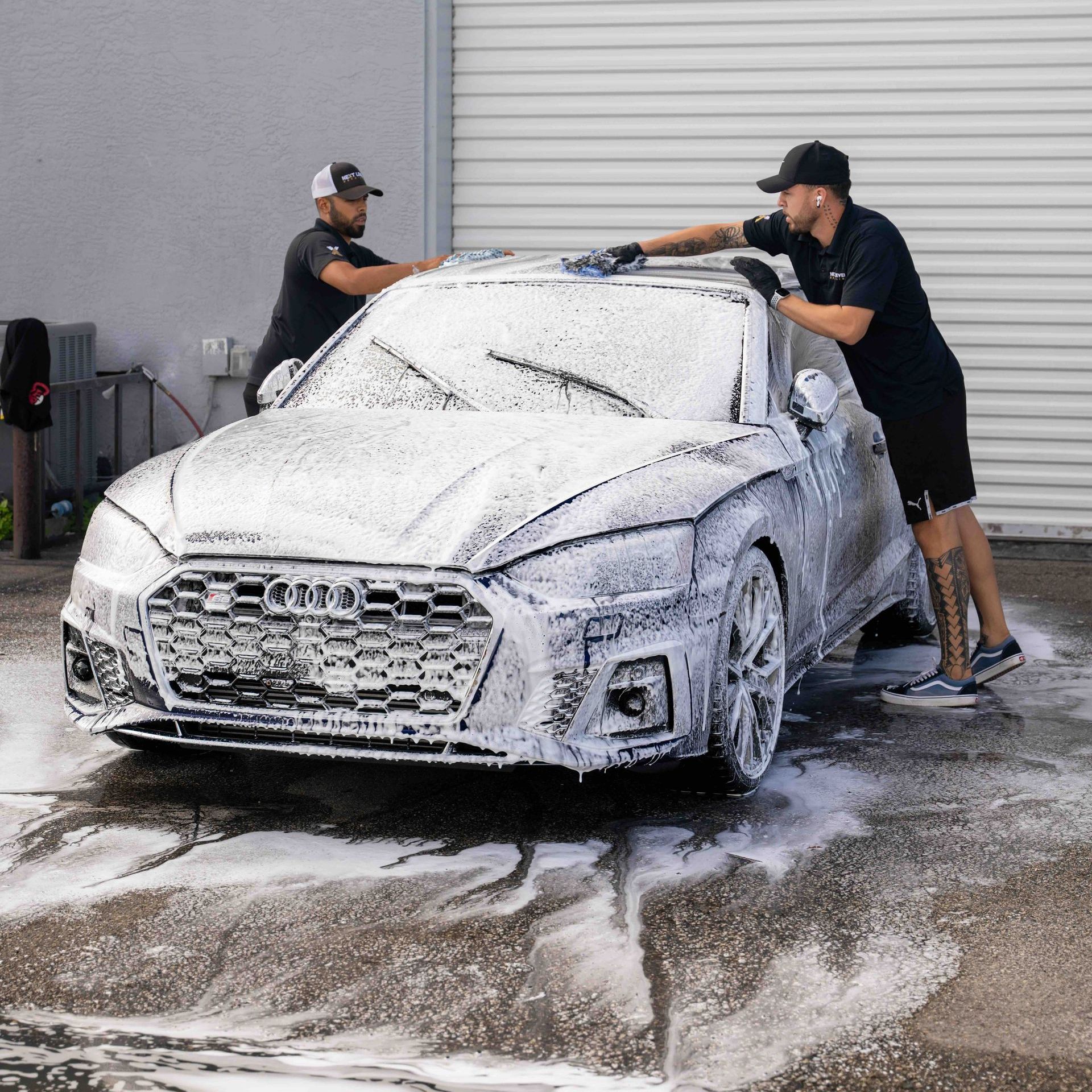 Two men are washing a car with foam in a parking lot.