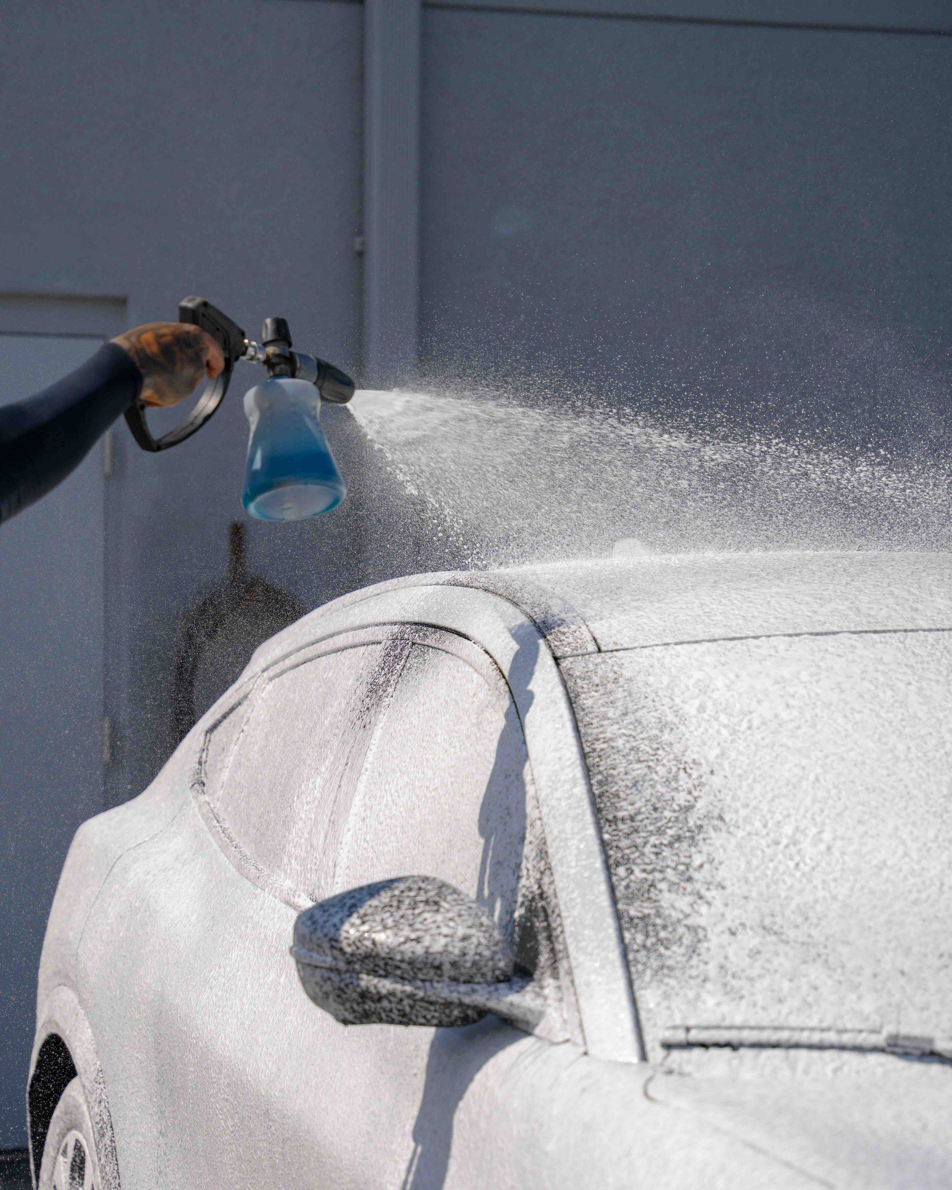 A person is spraying foam on a car with a spray bottle.
