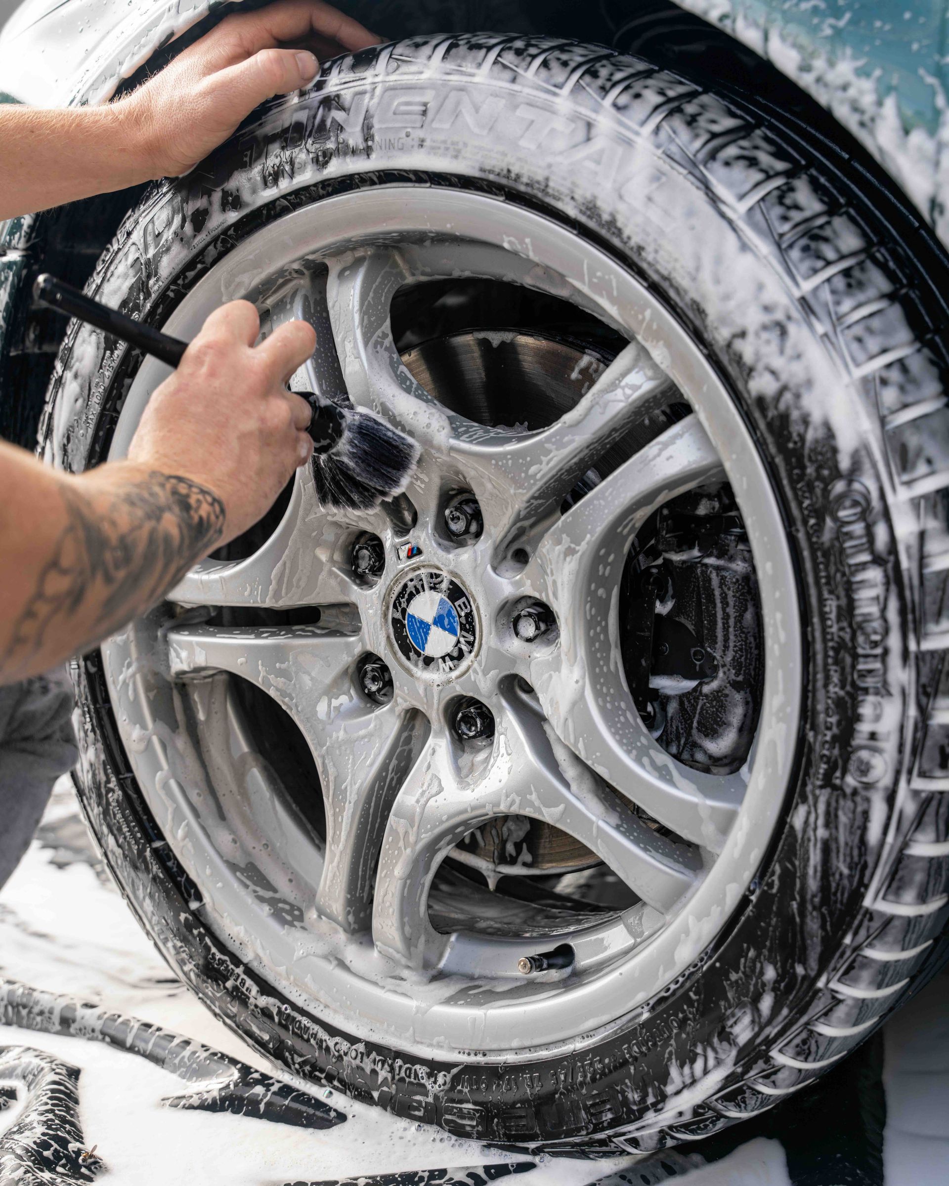 A man is cleaning a bmw wheel with a brush.
