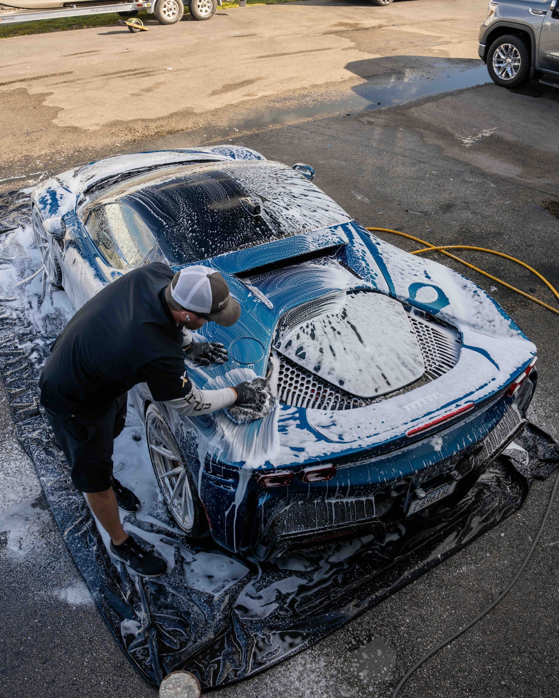 A man is washing a blue sports car with foam.