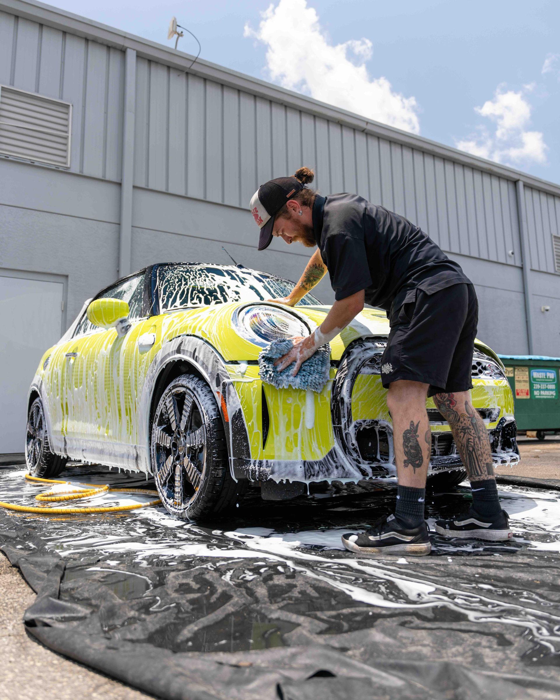 A man is washing a yellow car in front of a building.