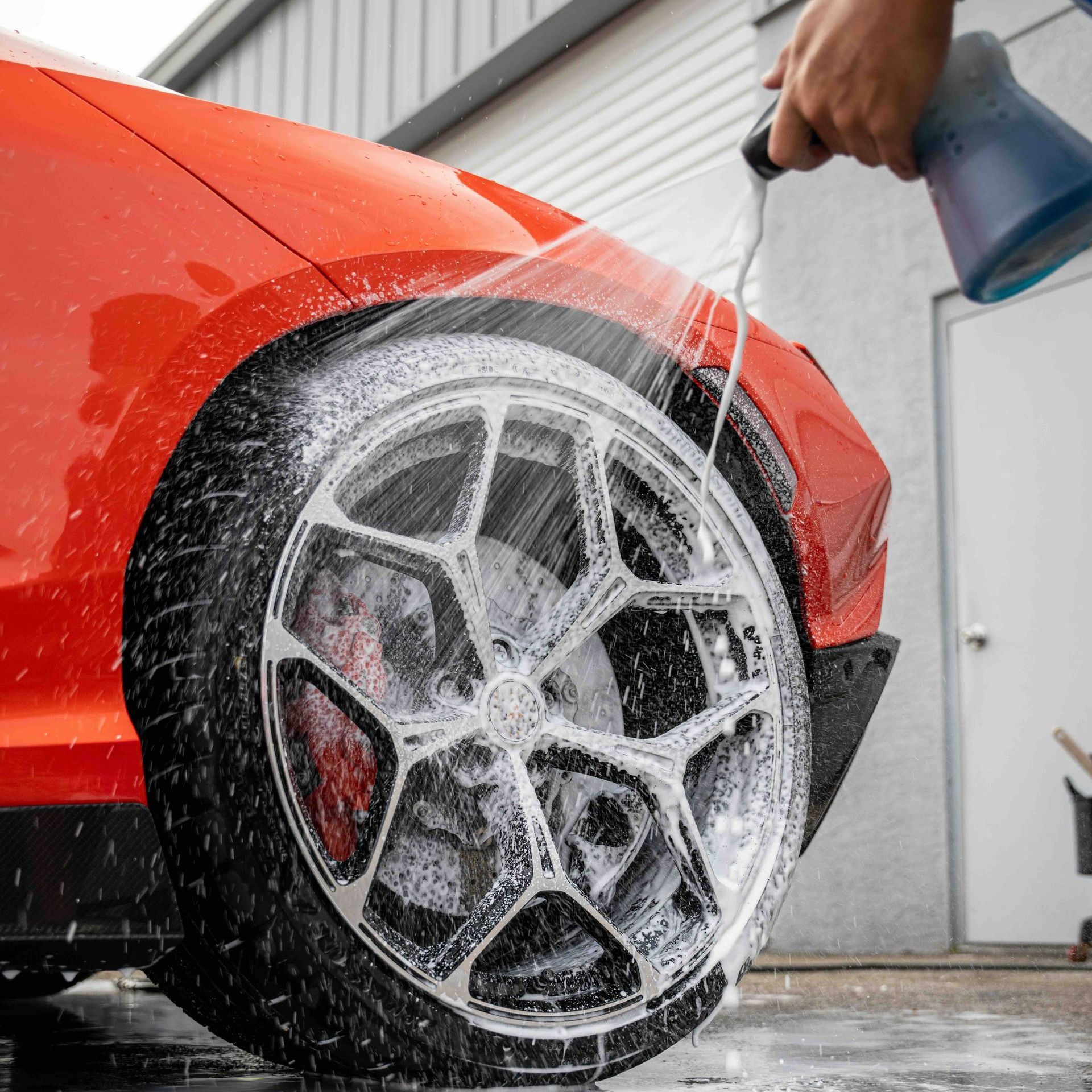 A person is washing a red car with a hose