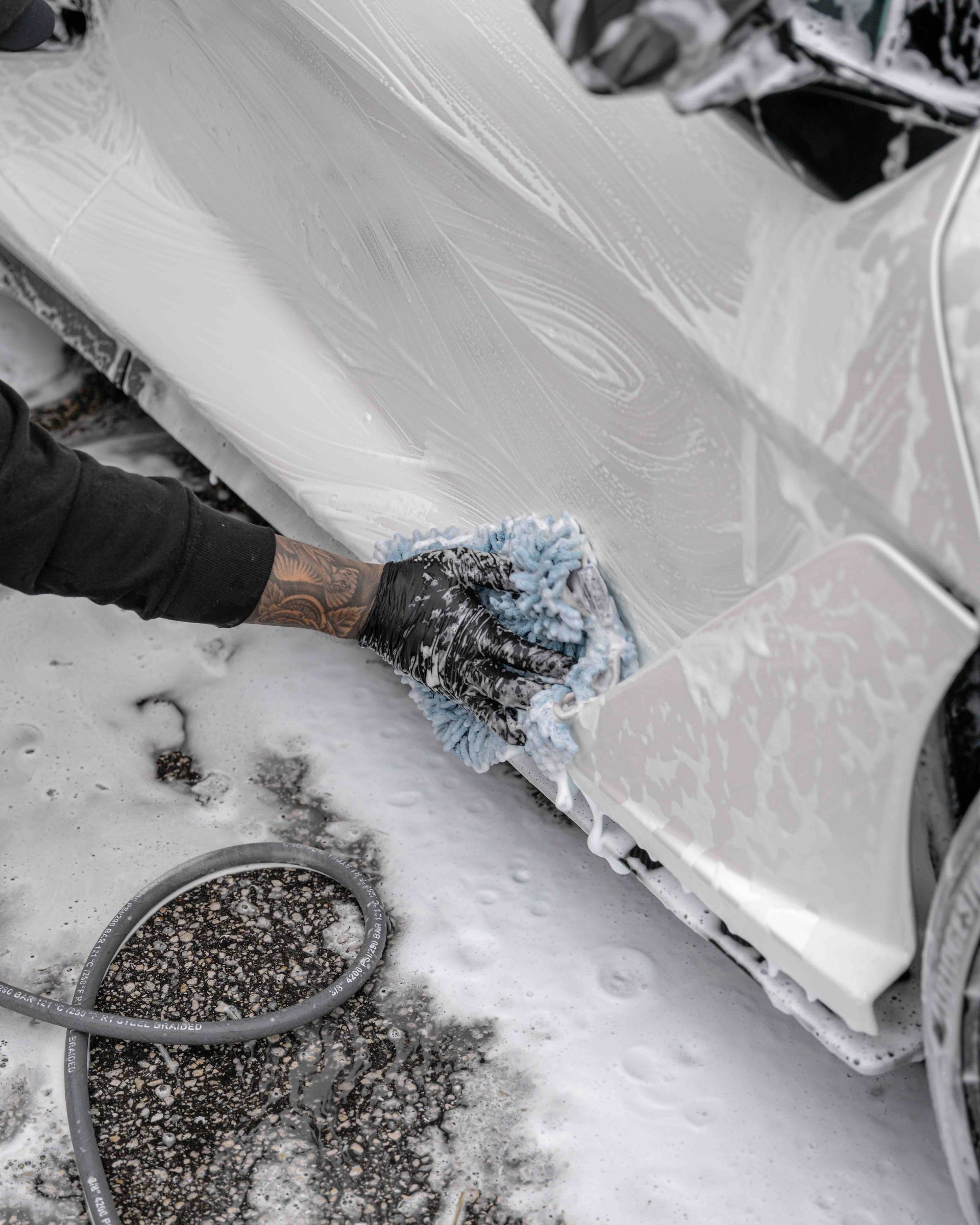 A person is washing a white car with a sponge.