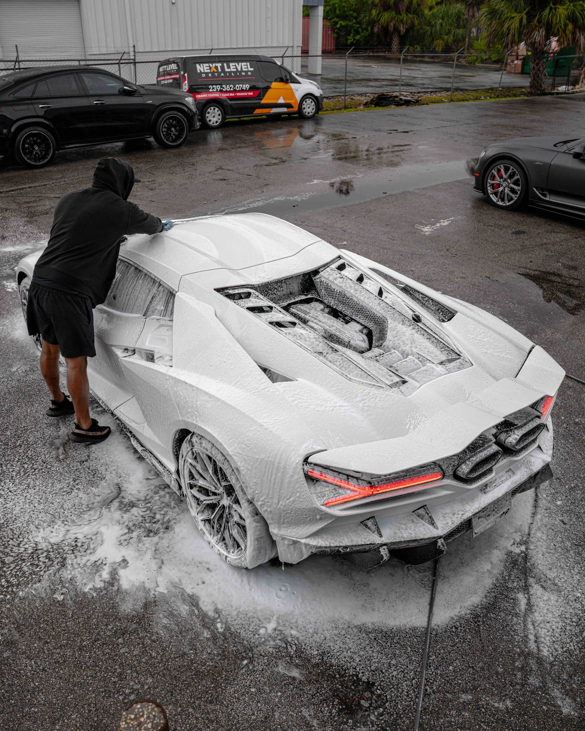 A man is washing a white sports car with foam.
