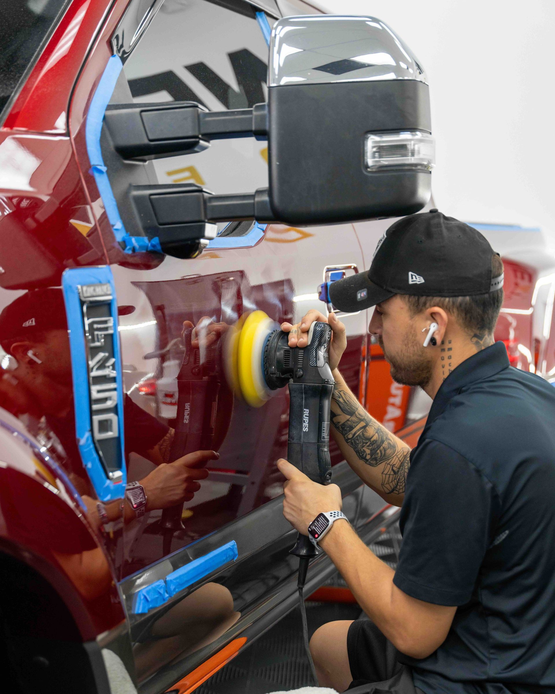 A man is polishing a red truck with a polisher.
