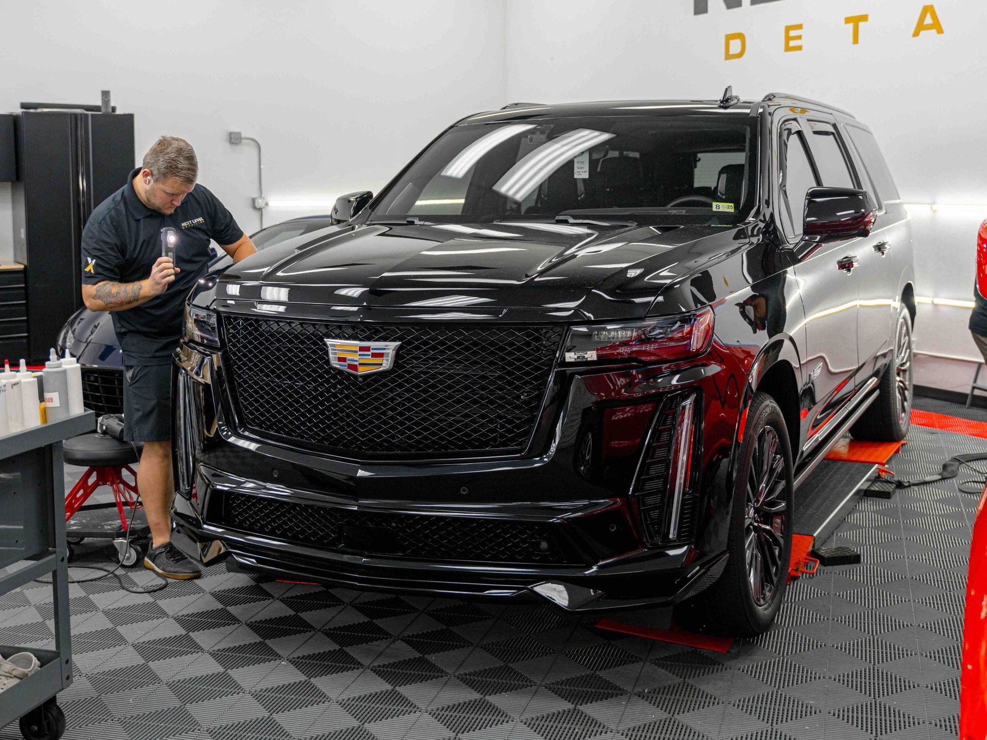 A man is working on a black cadillac escalade in a garage.