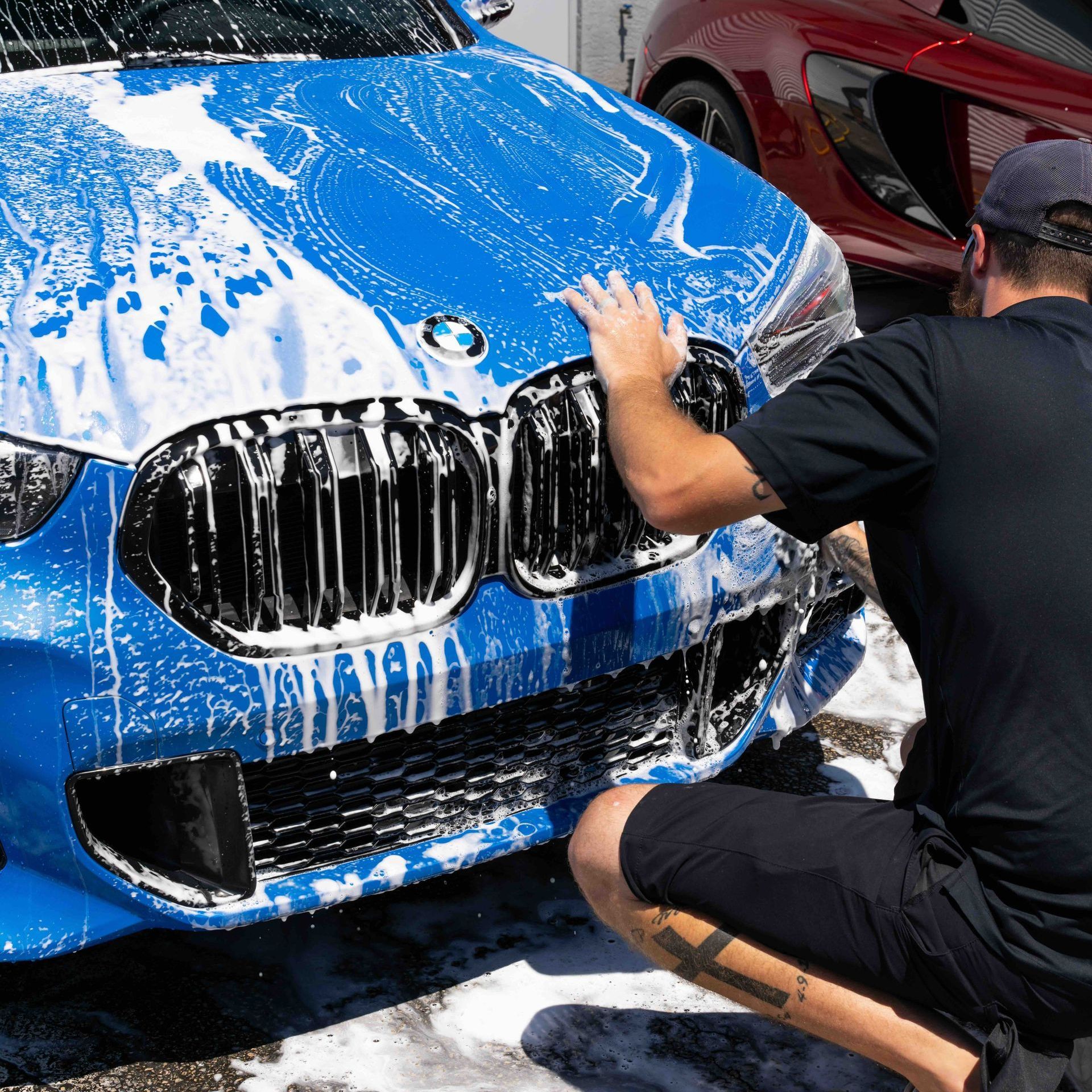 A man is kneeling down to wash a blue bmw