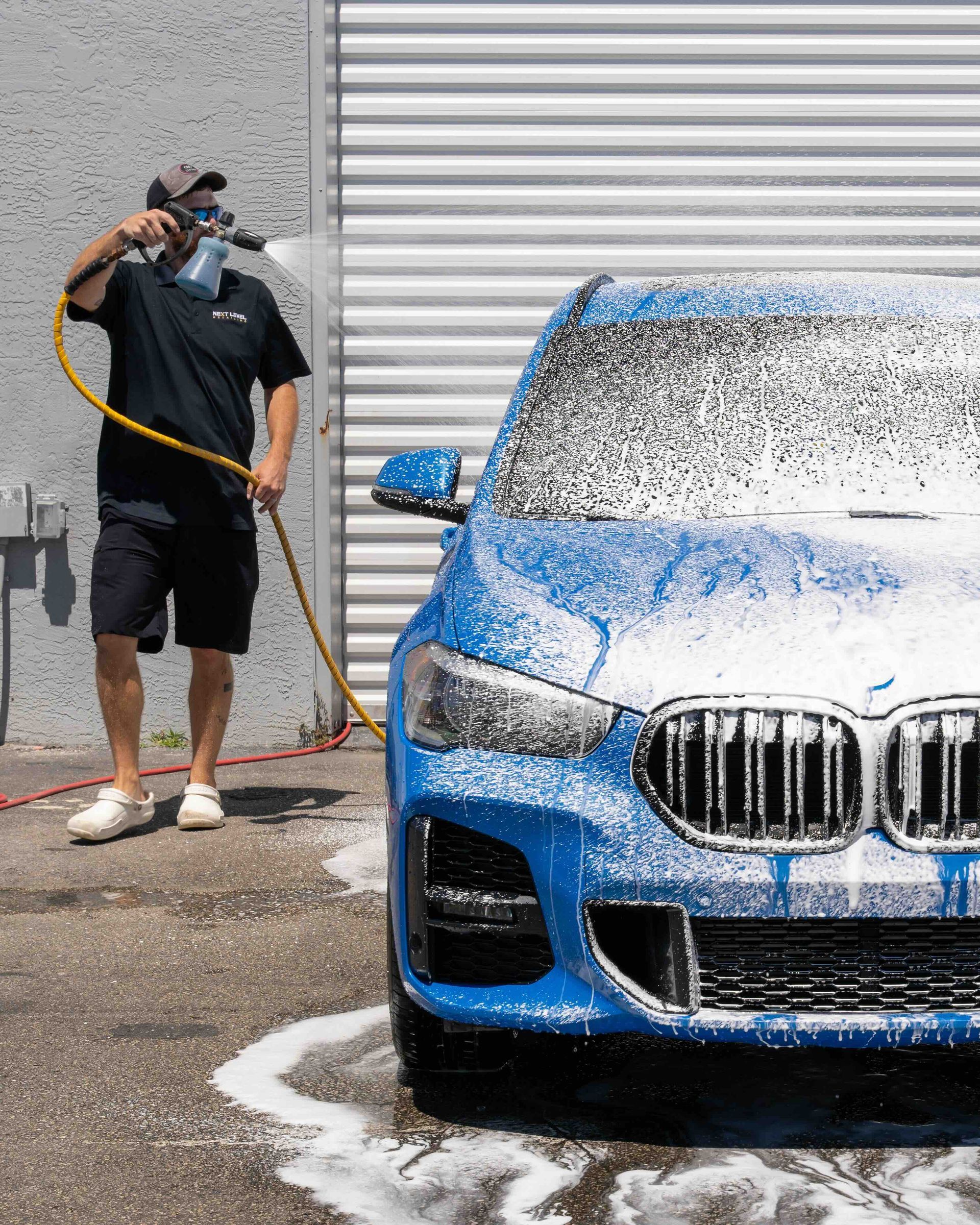 A man is washing a blue car with a hose.