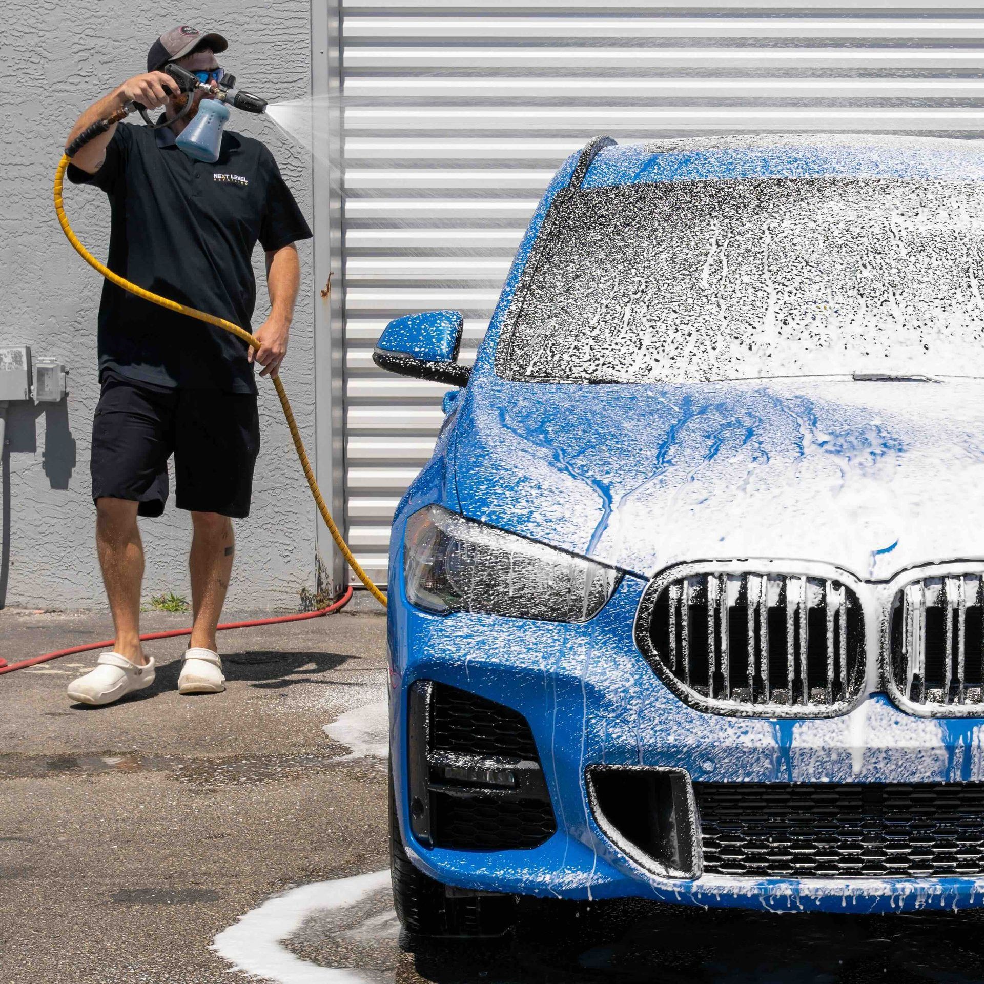 A man is washing a blue bmw with a hose.