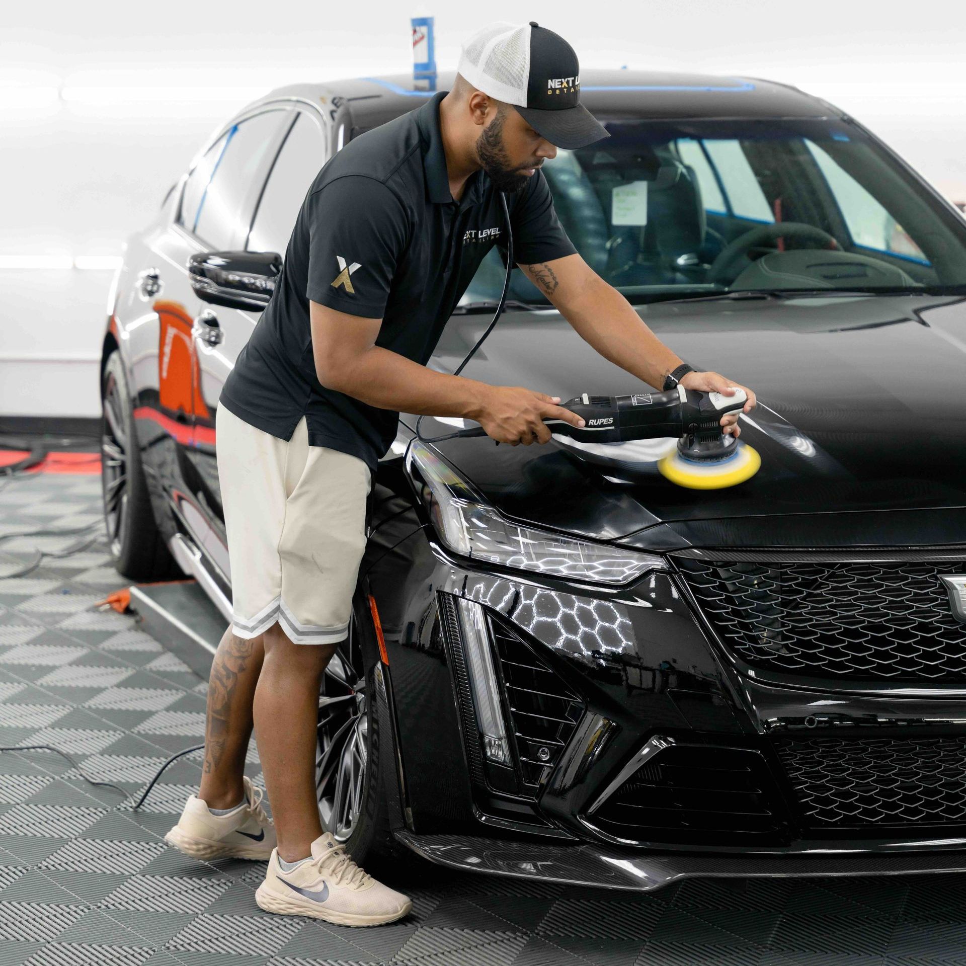 A man is polishing the hood of a black car.