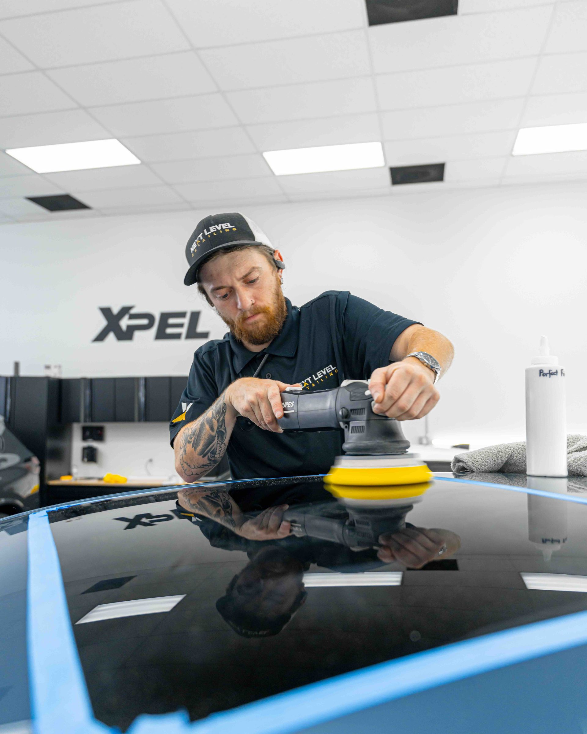 A man is polishing the roof of a car with a machine.