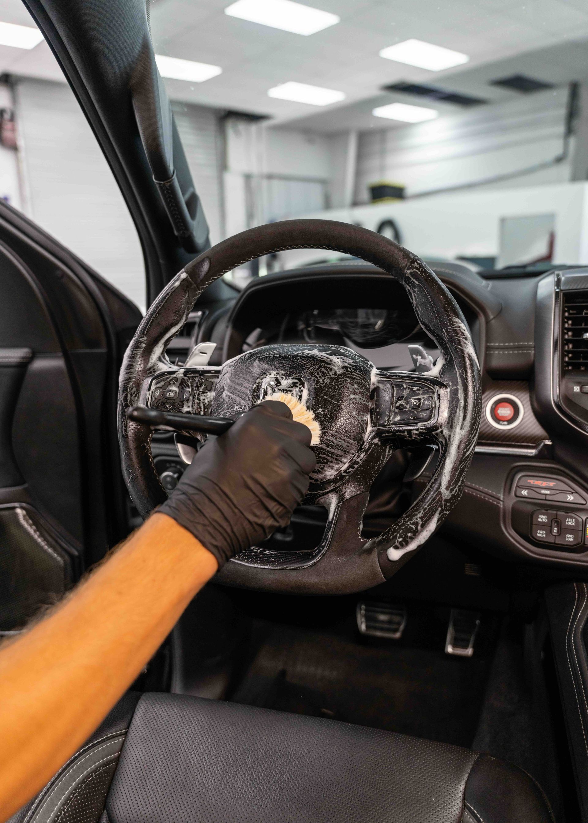 A person is cleaning the steering wheel of a car with a sponge.