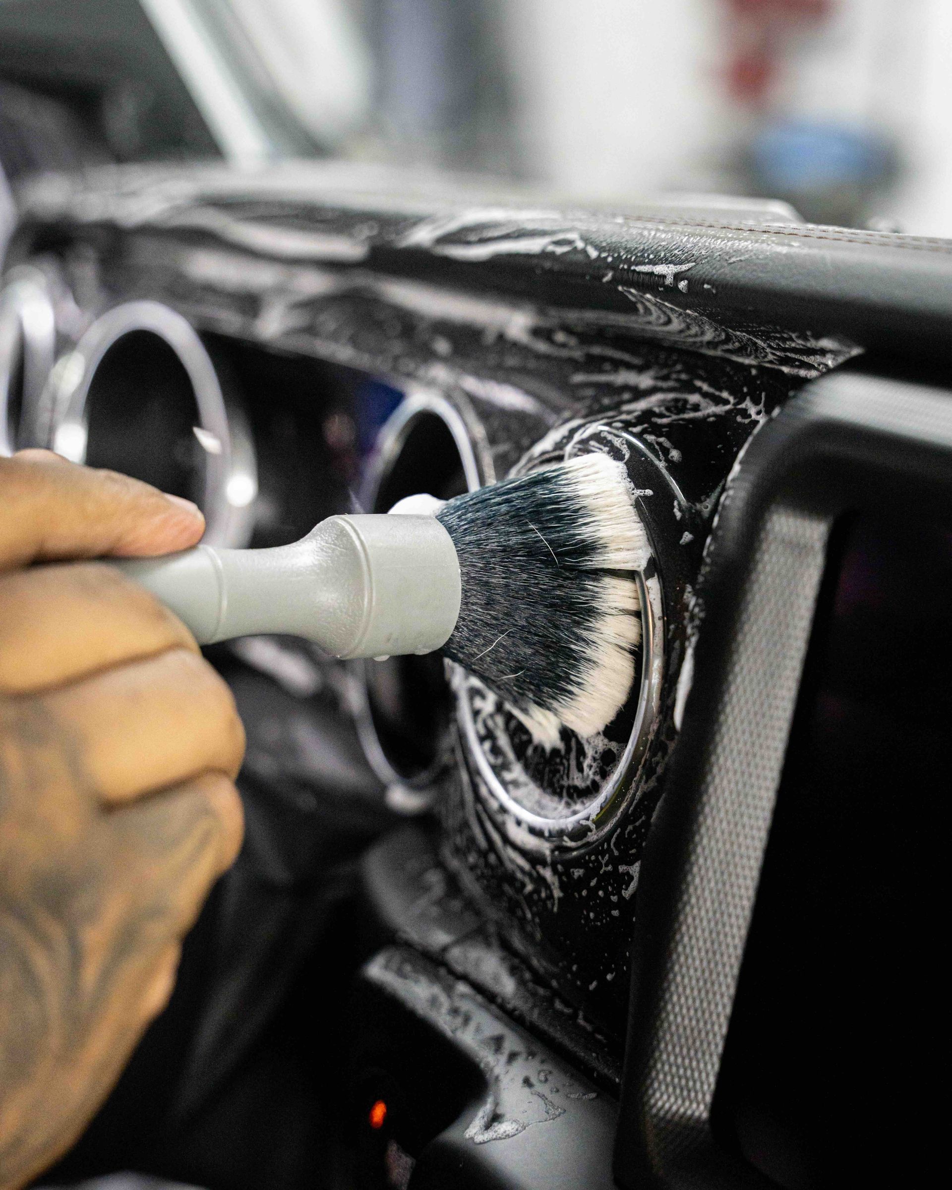 A person is cleaning the dashboard of a car with a brush.