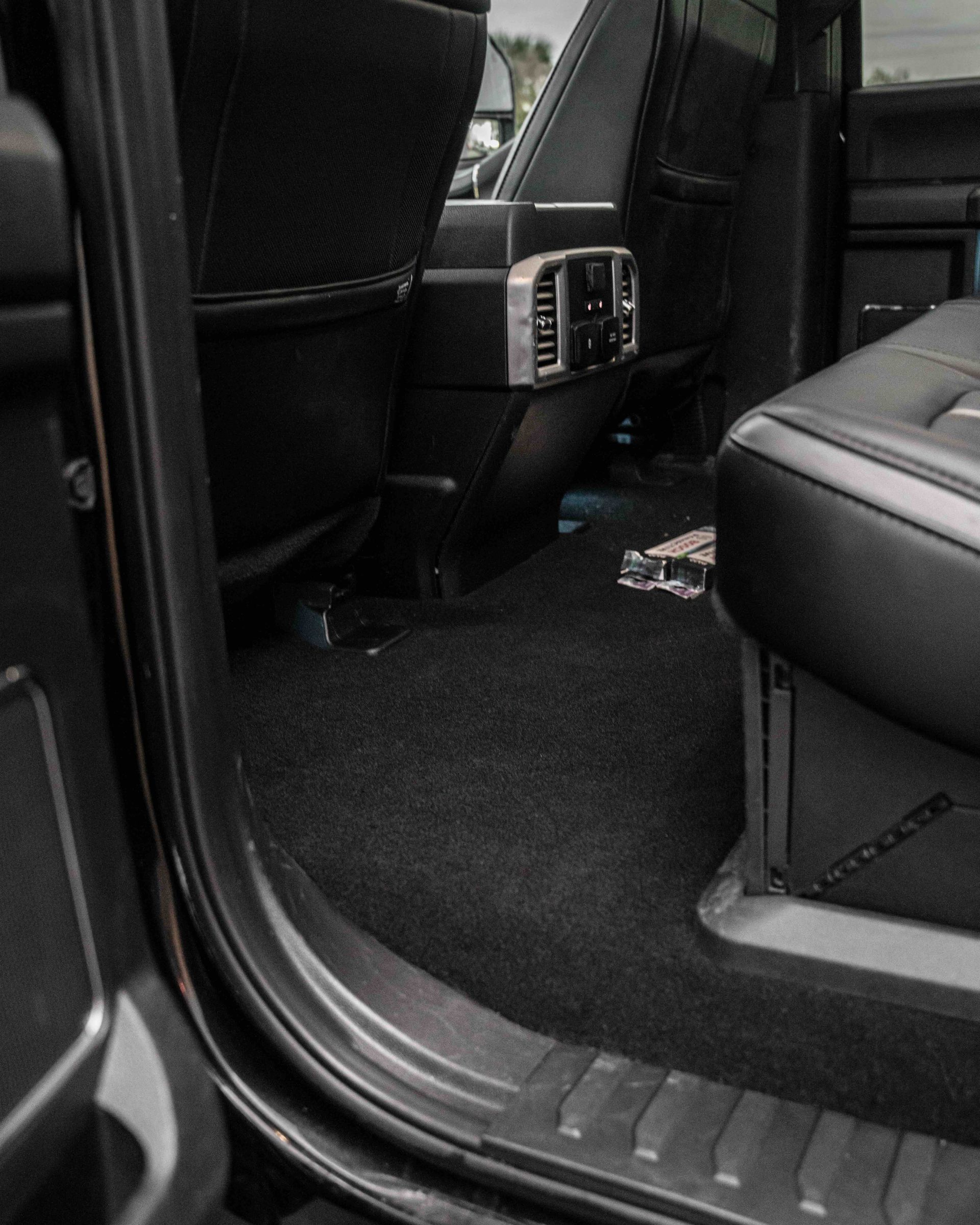 The inside of a black truck with the door open and the back seats.