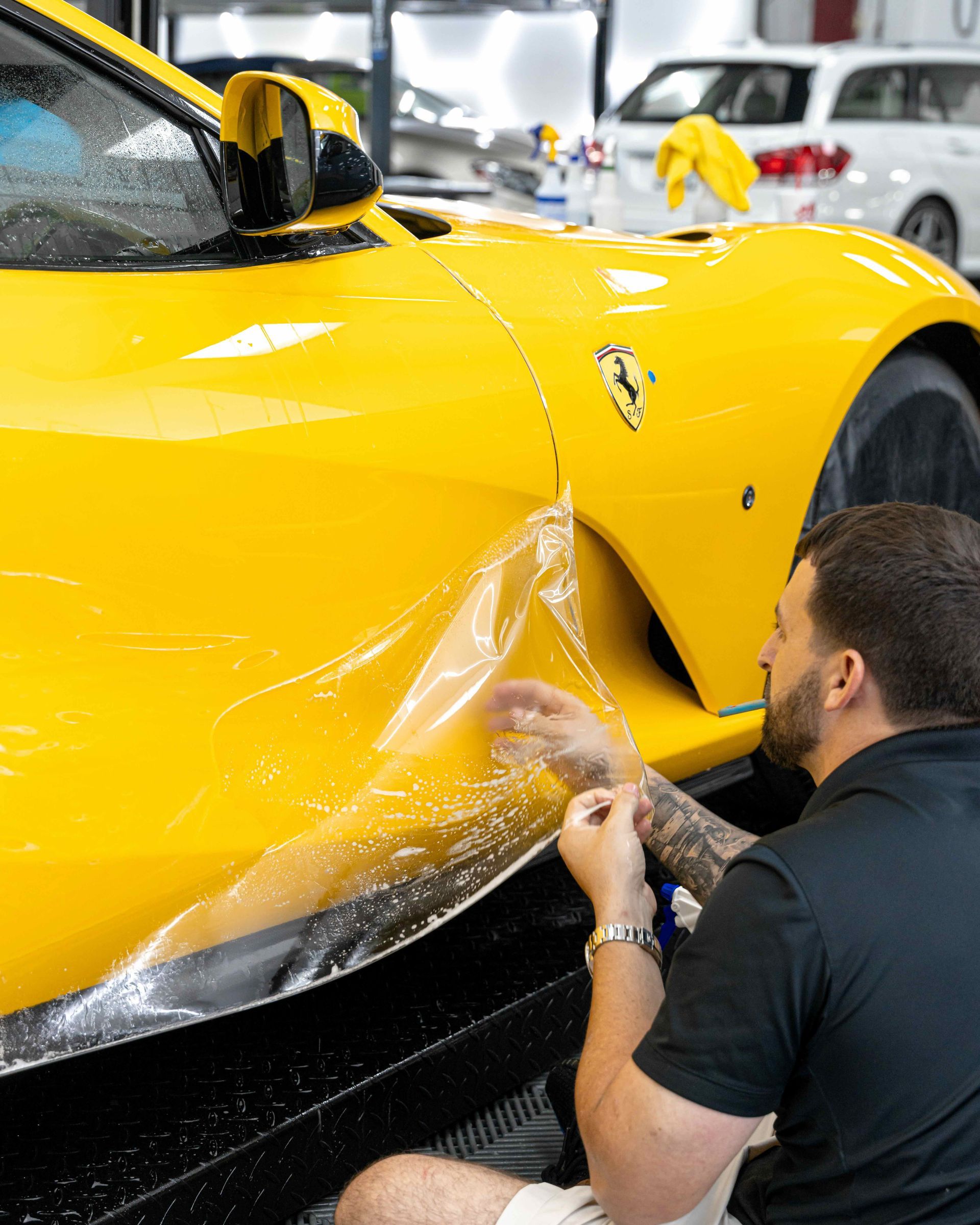 A man is wrapping a yellow sports car with plastic wrap.