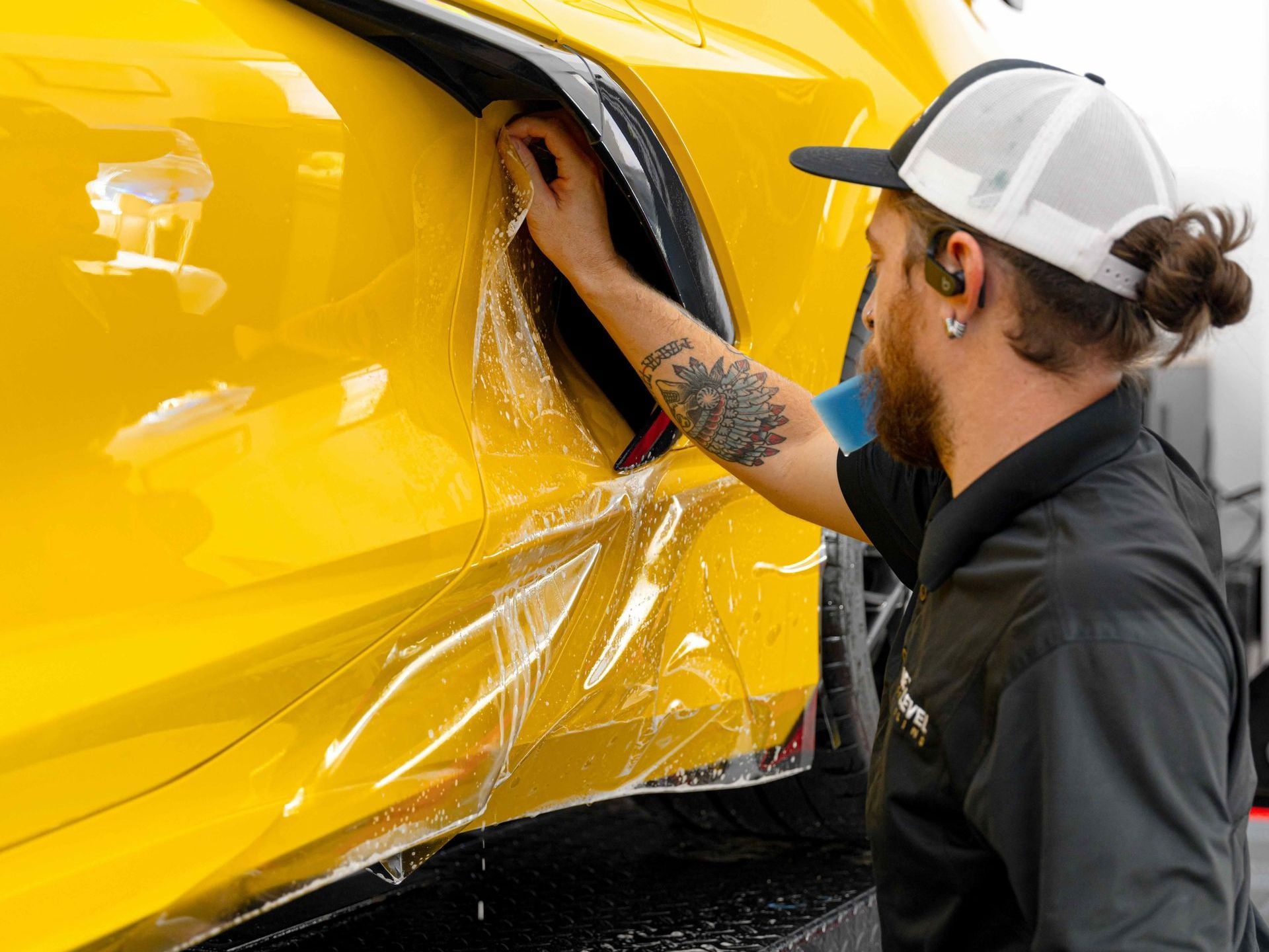 A man is wrapping a yellow car with plastic wrap.