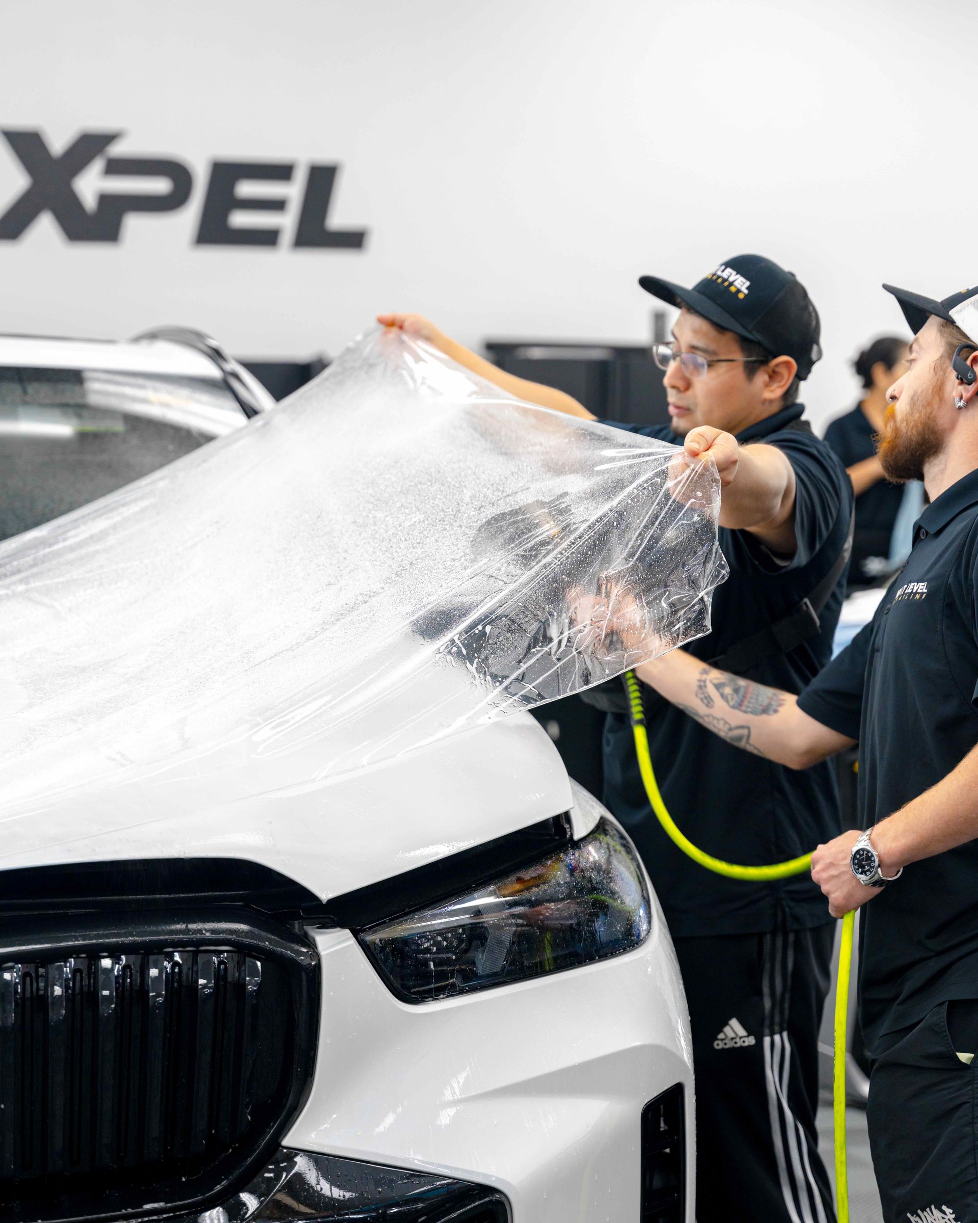 A group of men are wrapping a white car with plastic wrap.