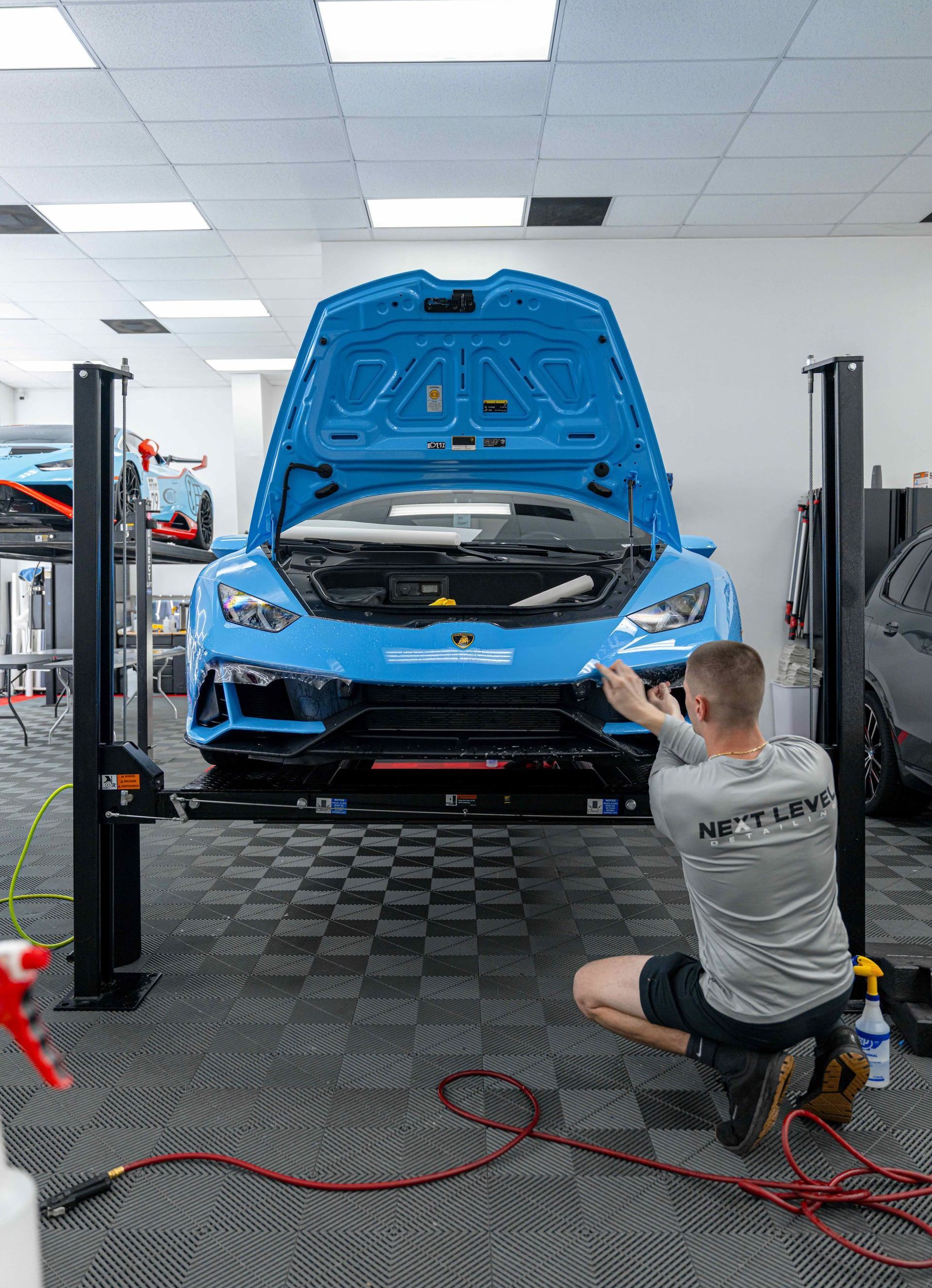 A man is kneeling down in front of a blue car on a lift.