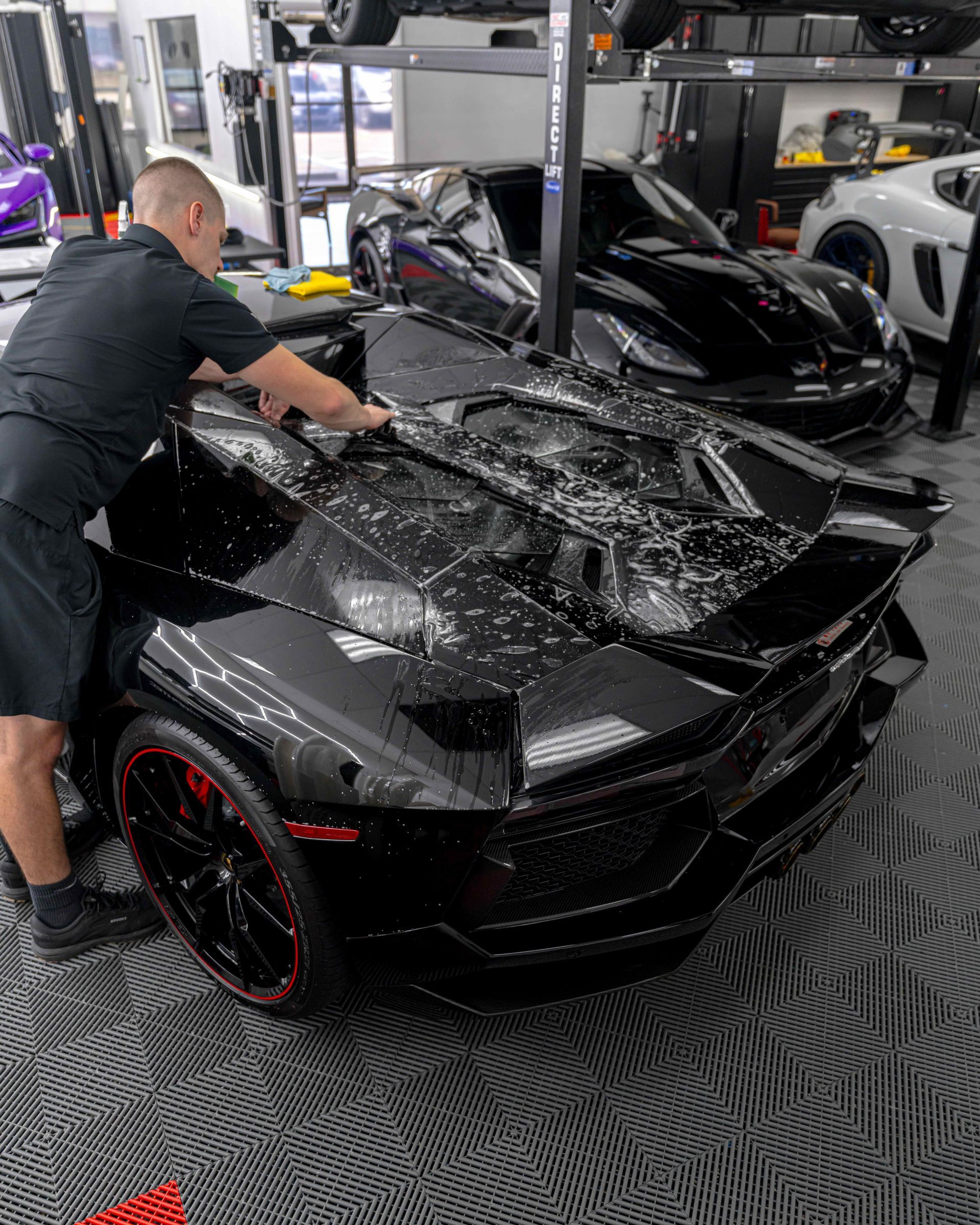 A man is working on a black sports car in a garage.