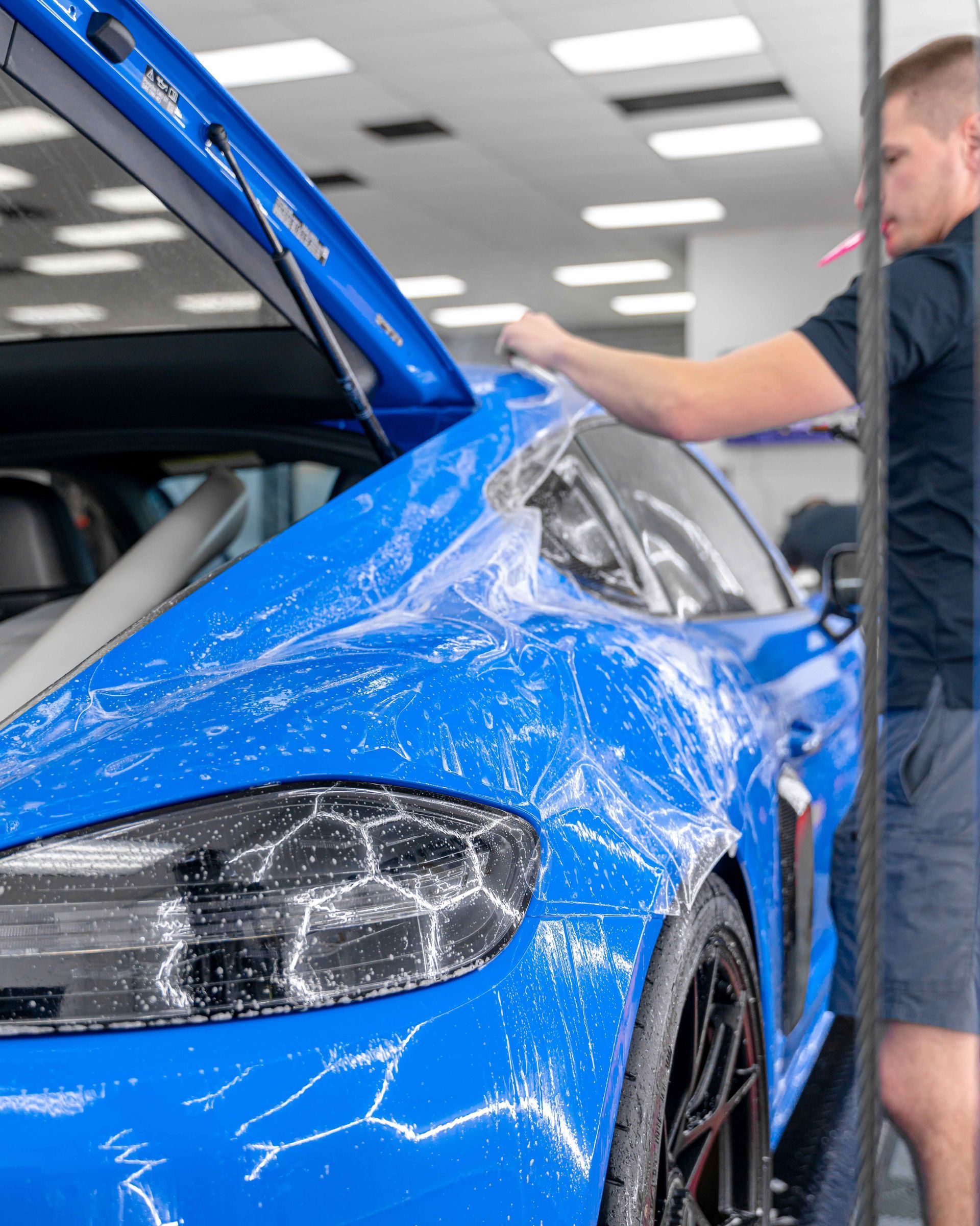 A man is wrapping a blue car with plastic