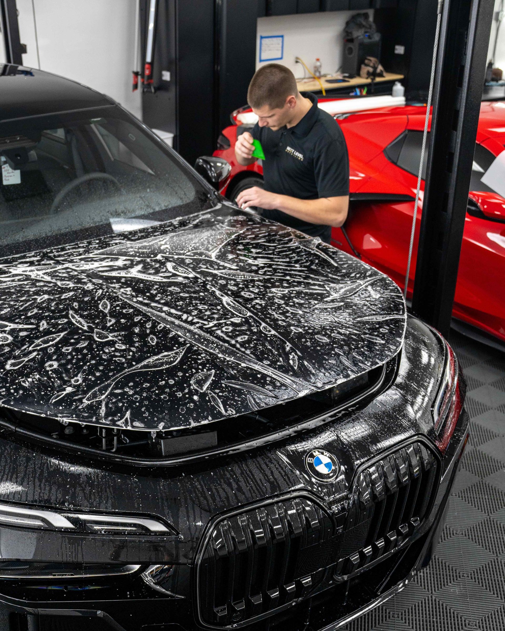 A man is cleaning the hood of a black car in a garage.