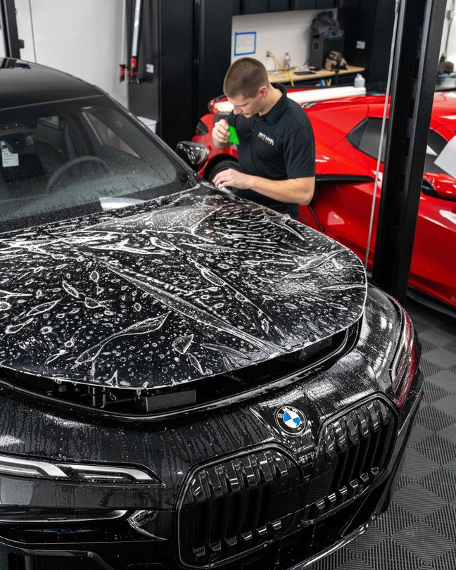A man is cleaning the hood of a black car in a garage.