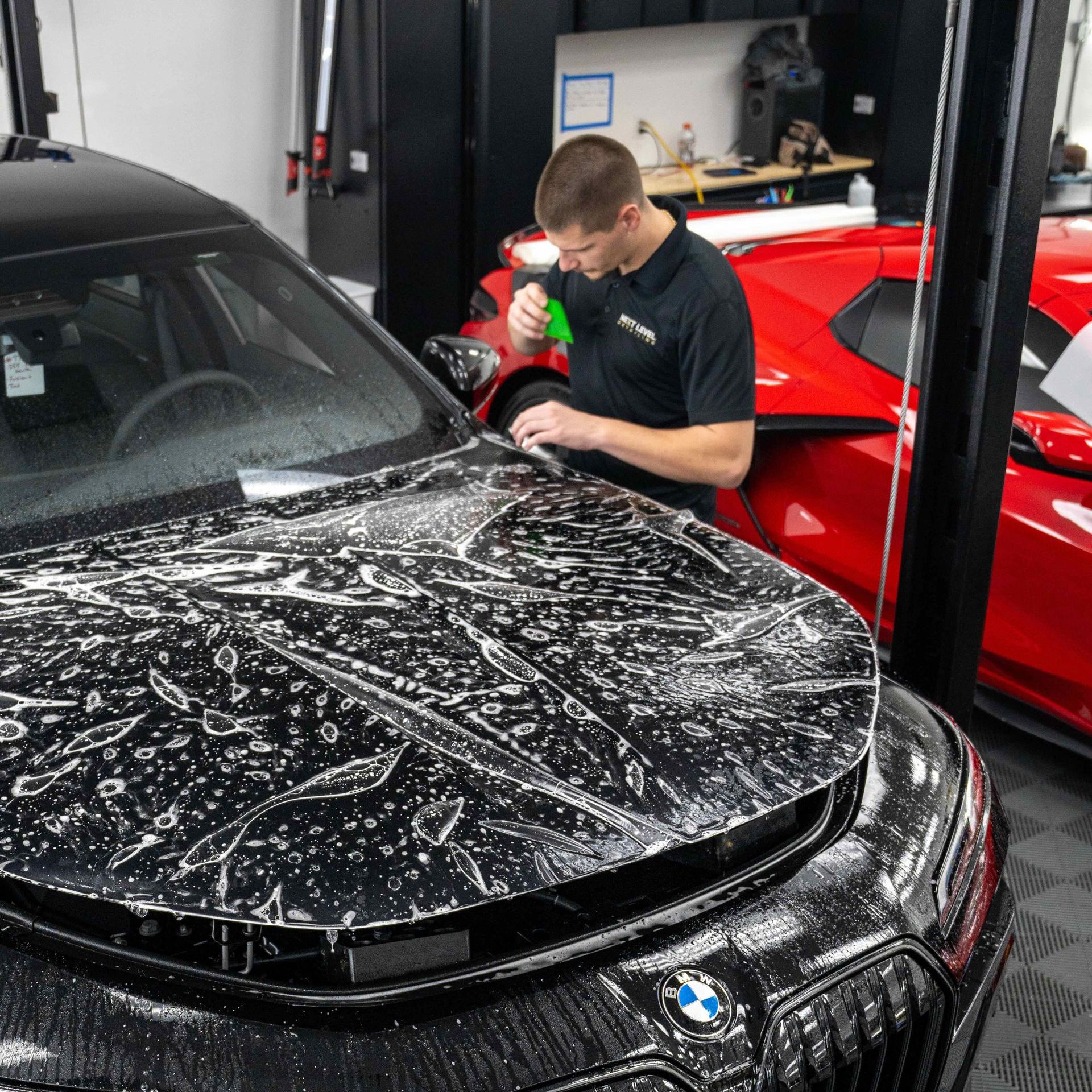 A man is cleaning the hood of a black car in a garage.