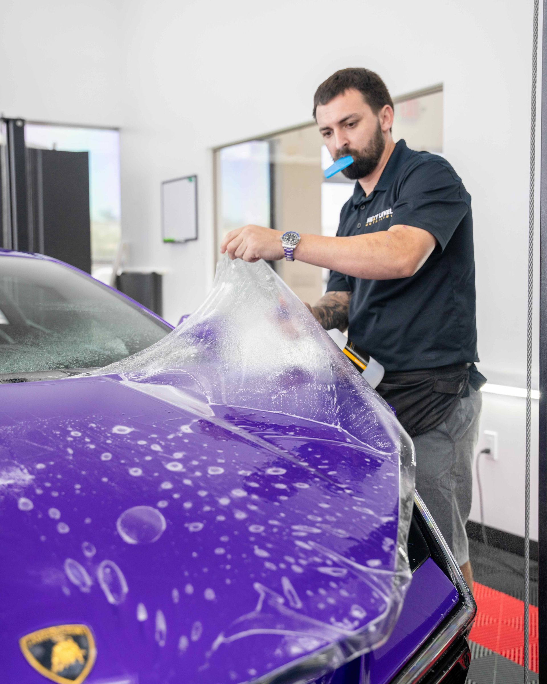 A man is covering a purple car with a plastic wrap.