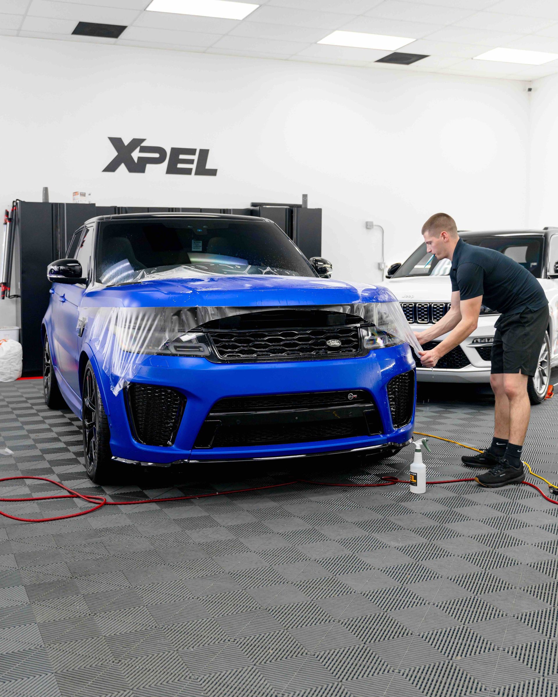 A man is wrapping a blue car in a garage.