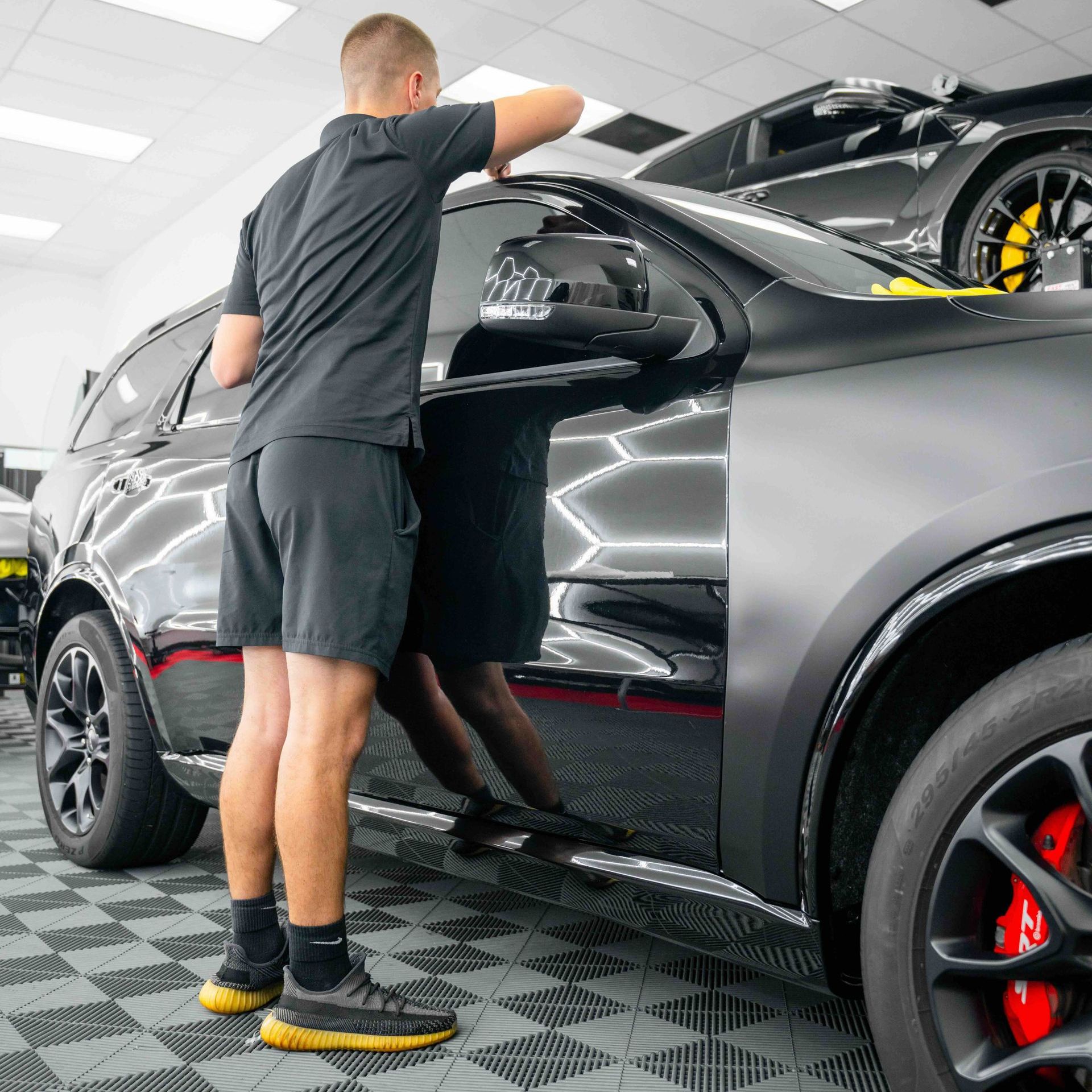 A man is standing next to a black car in a garage.