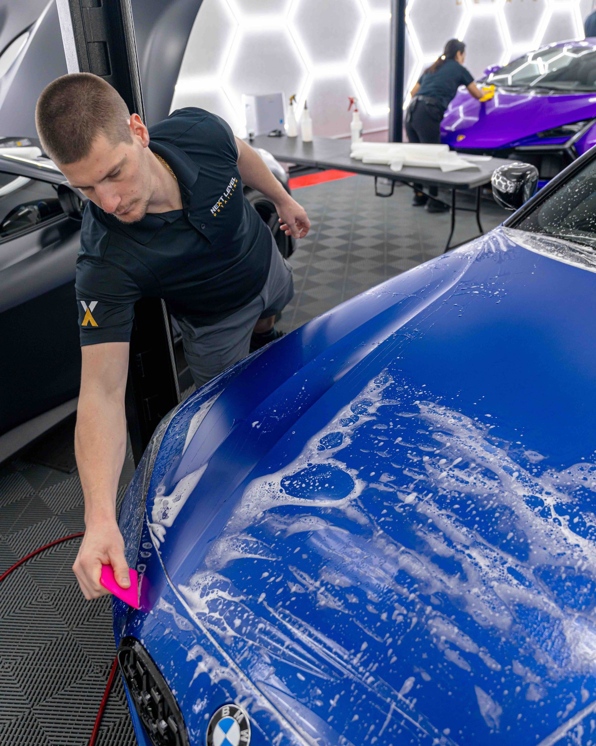 A man is cleaning the hood of a blue car.