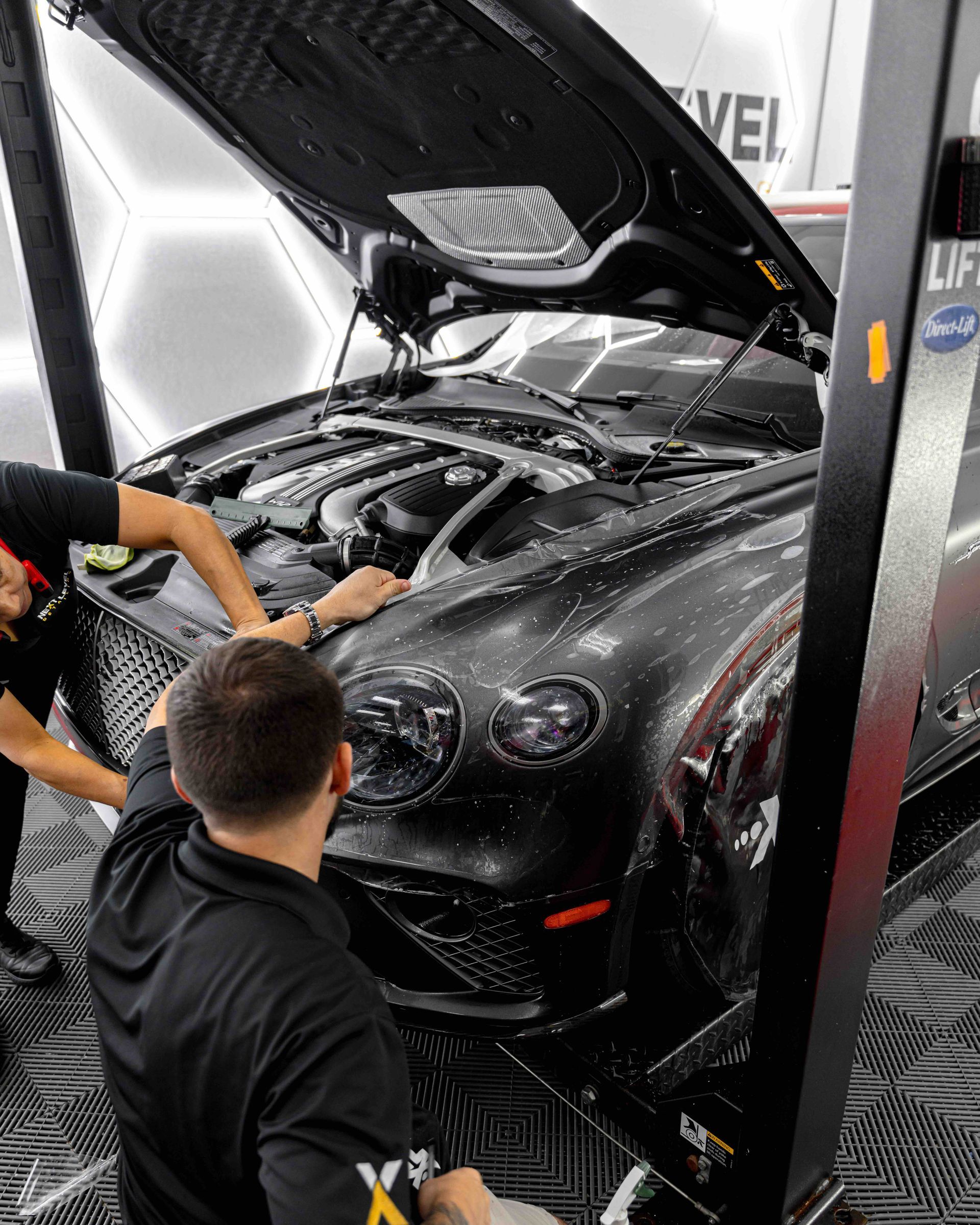 Two men are working on a black car with the hood open
