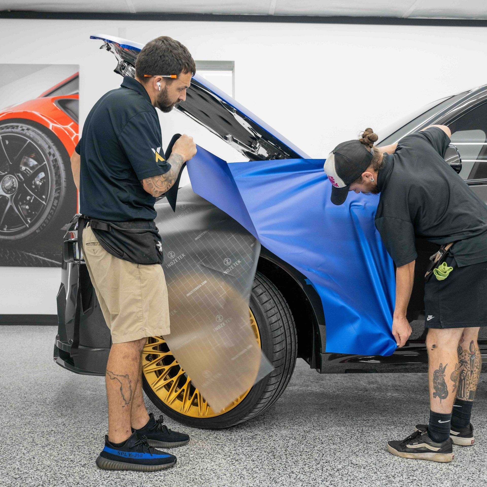 Two men are wrapping a car with a blue cloth.