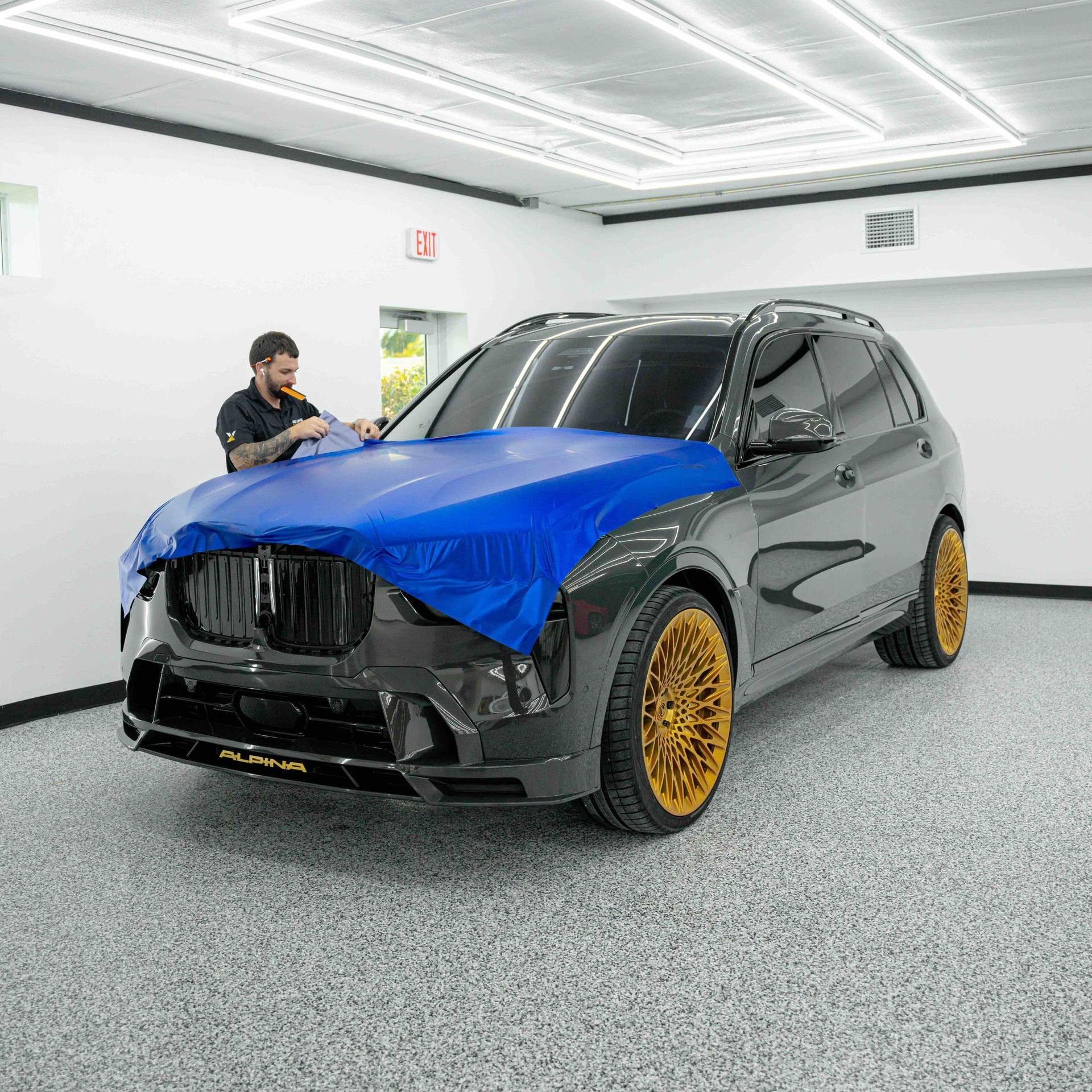 A man is wrapping a car with a blue cloth in a garage.