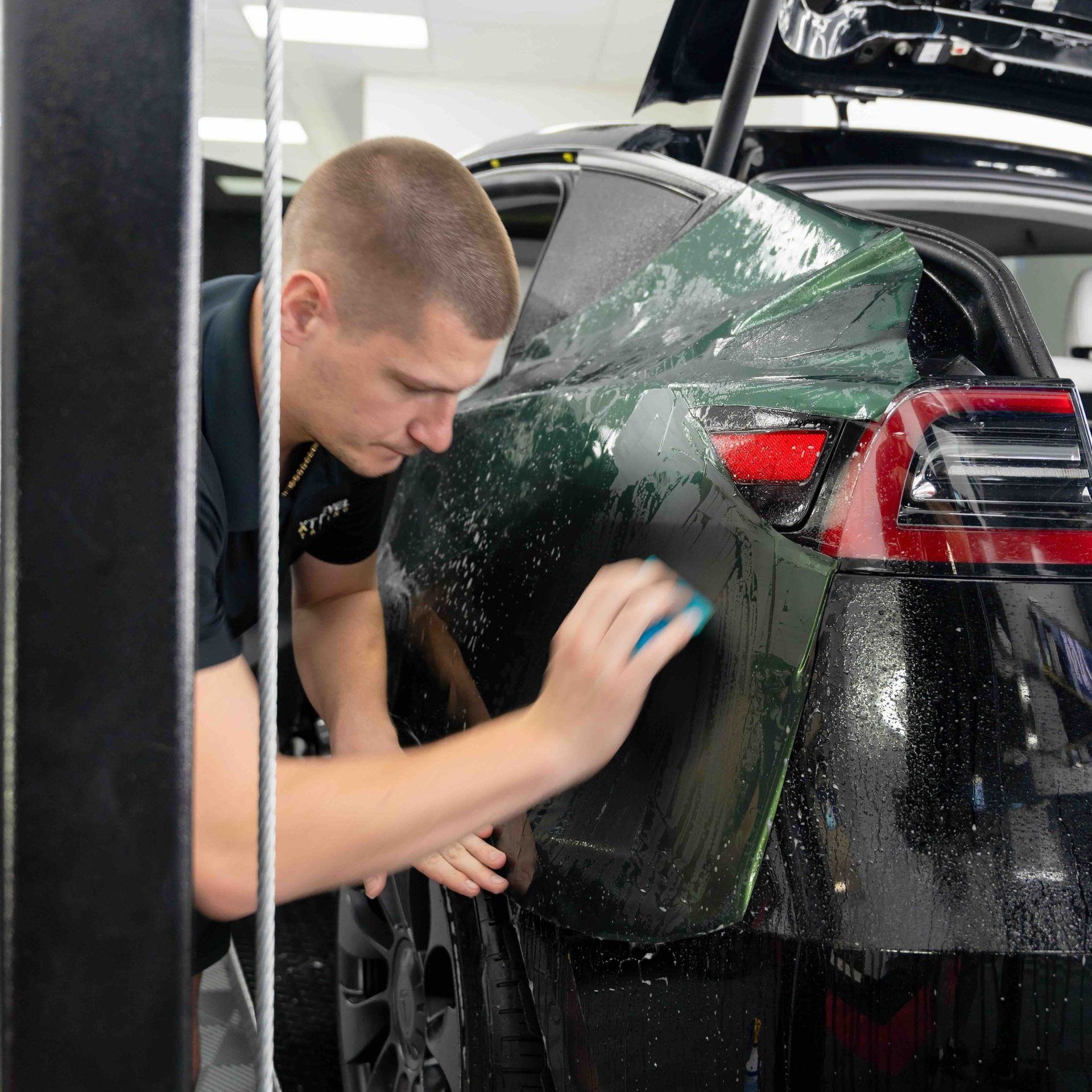 A man is cleaning the back of a car with a sponge.