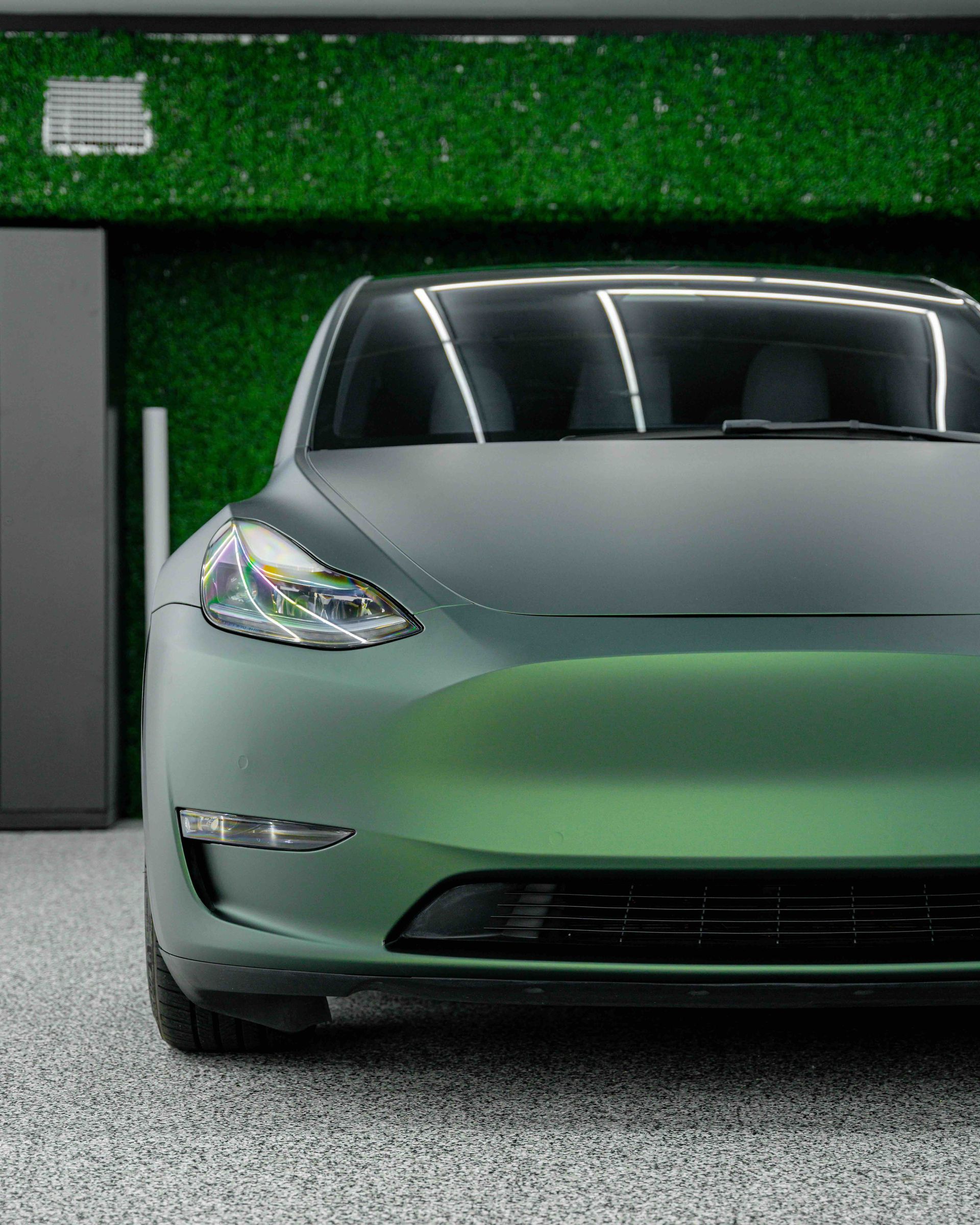 A green tesla model 3 is parked in a garage.